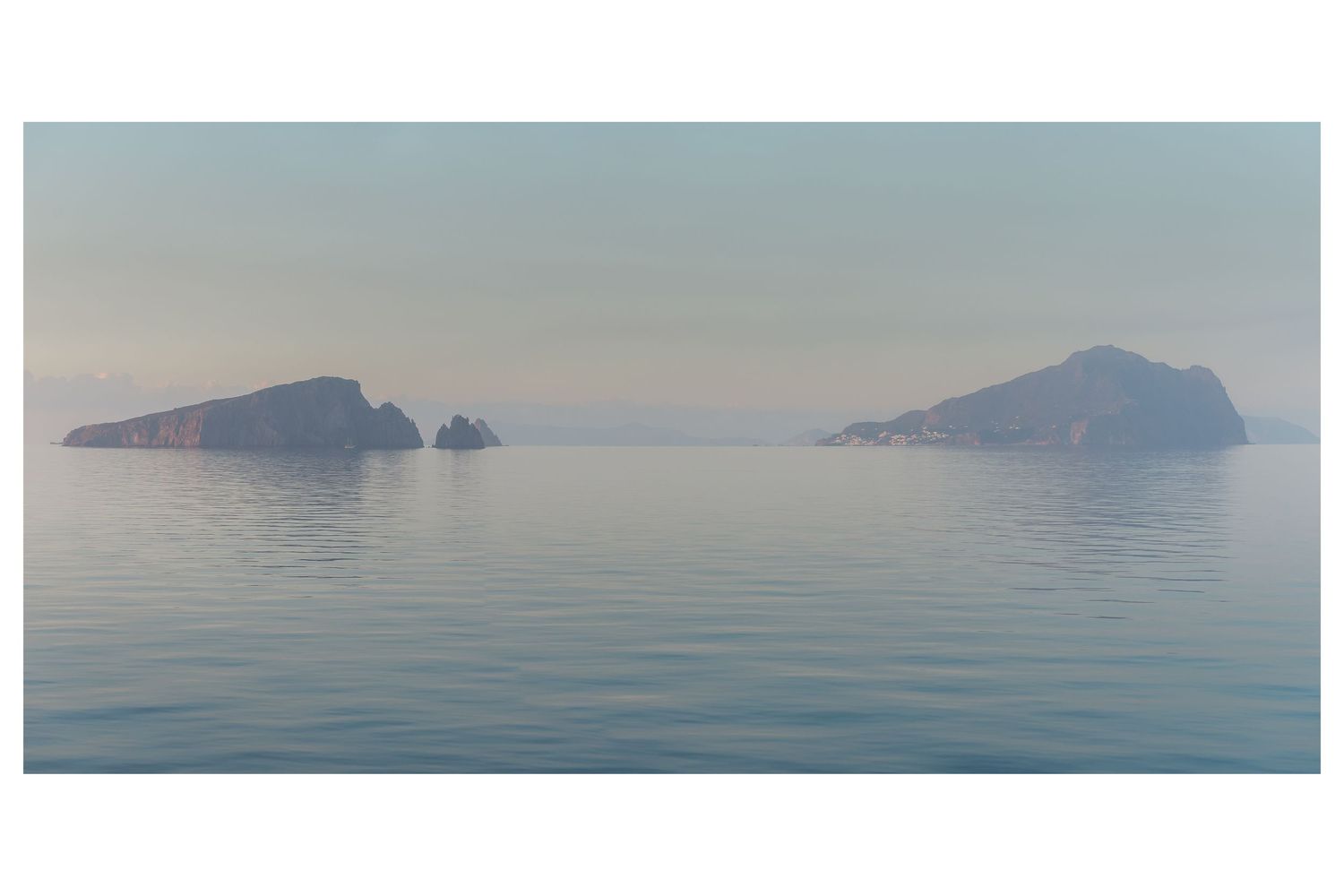Tranquil Mediterranean seascape with misty islands and mountains rising from calm waters at dawn.