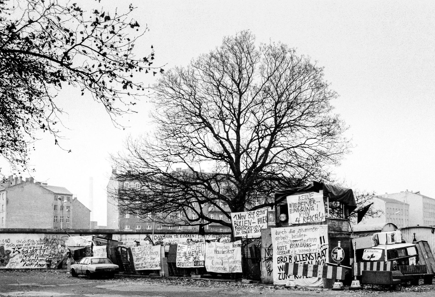 Panoramic view of the Berlin Wall area showing buildings and protest signs.