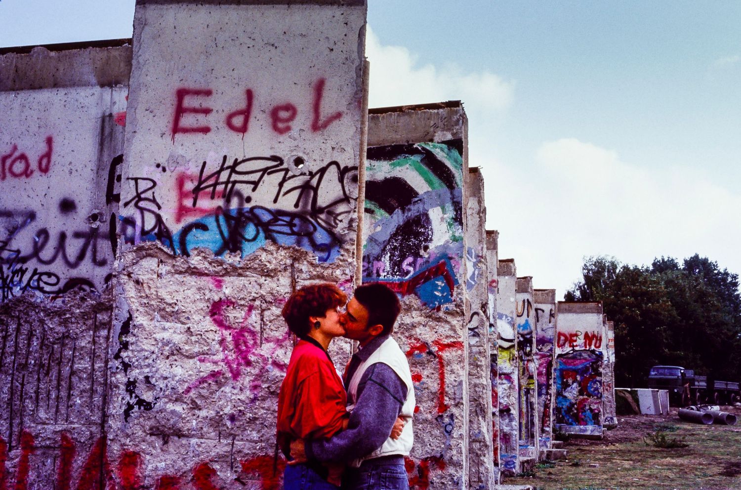 Section of the Berlin Wall with red graffiti and street art visible on its concrete surface.