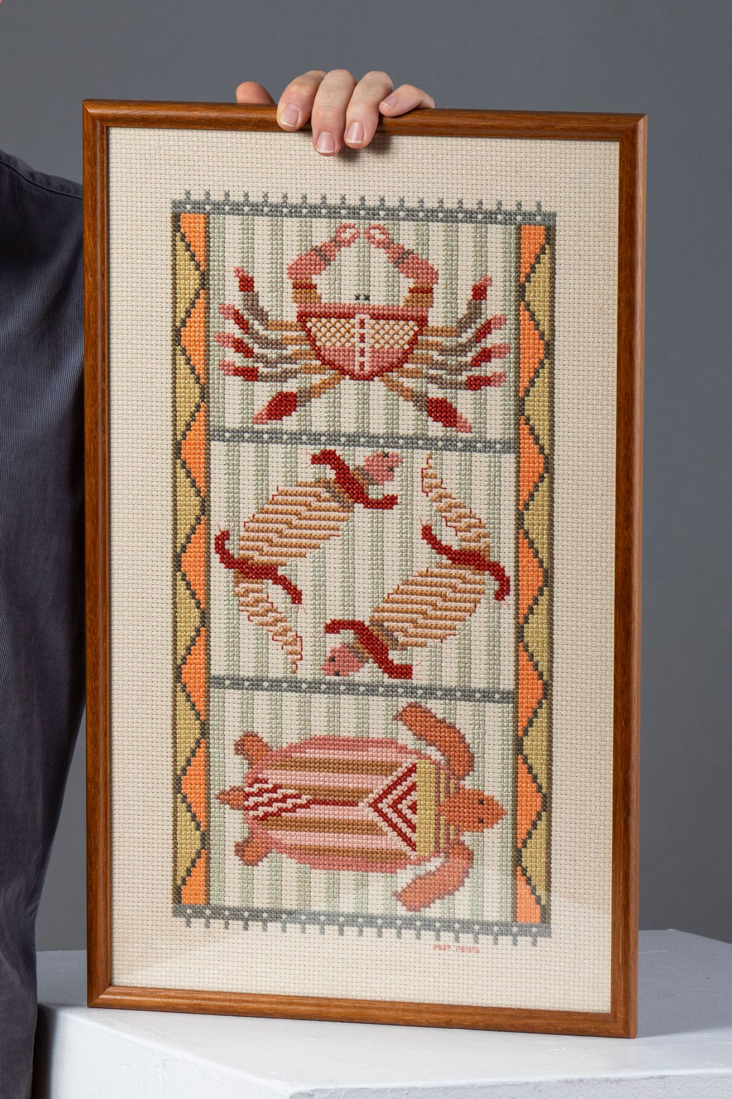 Four sequential photos show a framed cross-stitch artwork featuring red lobsters and crabs in a geometric coastal design pattern.