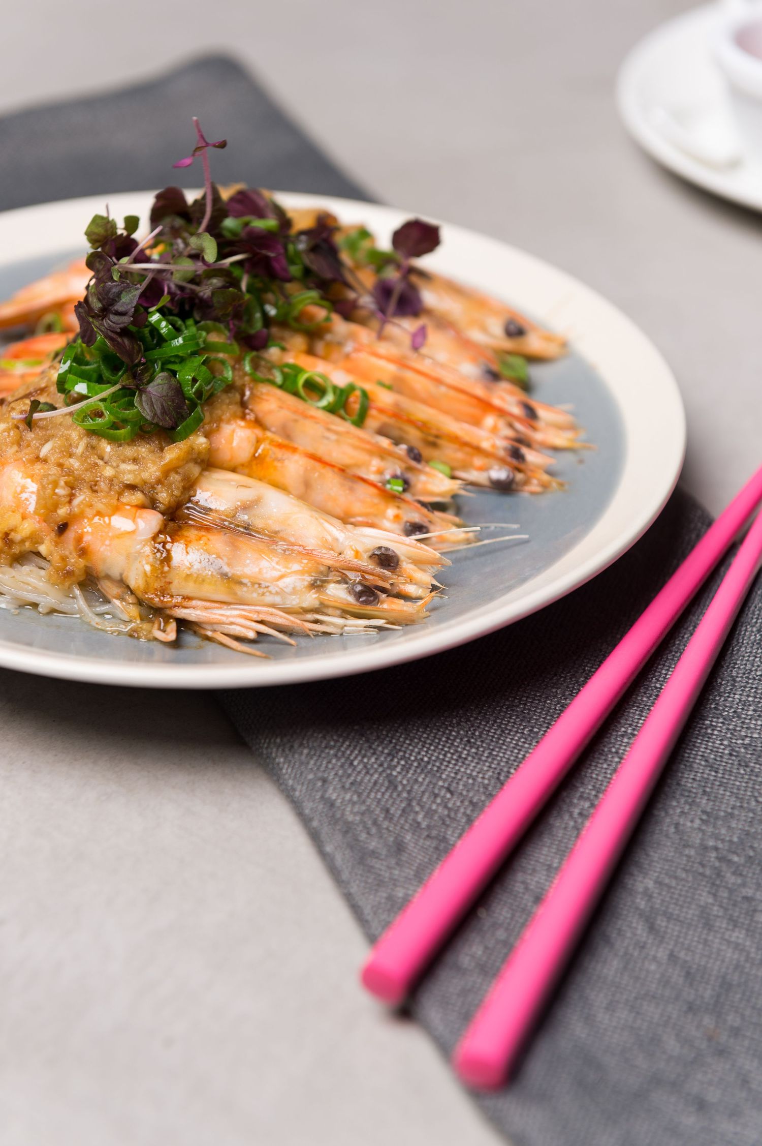 Grilled prawns garnished with fresh herbs and served with bright pink chopsticks.