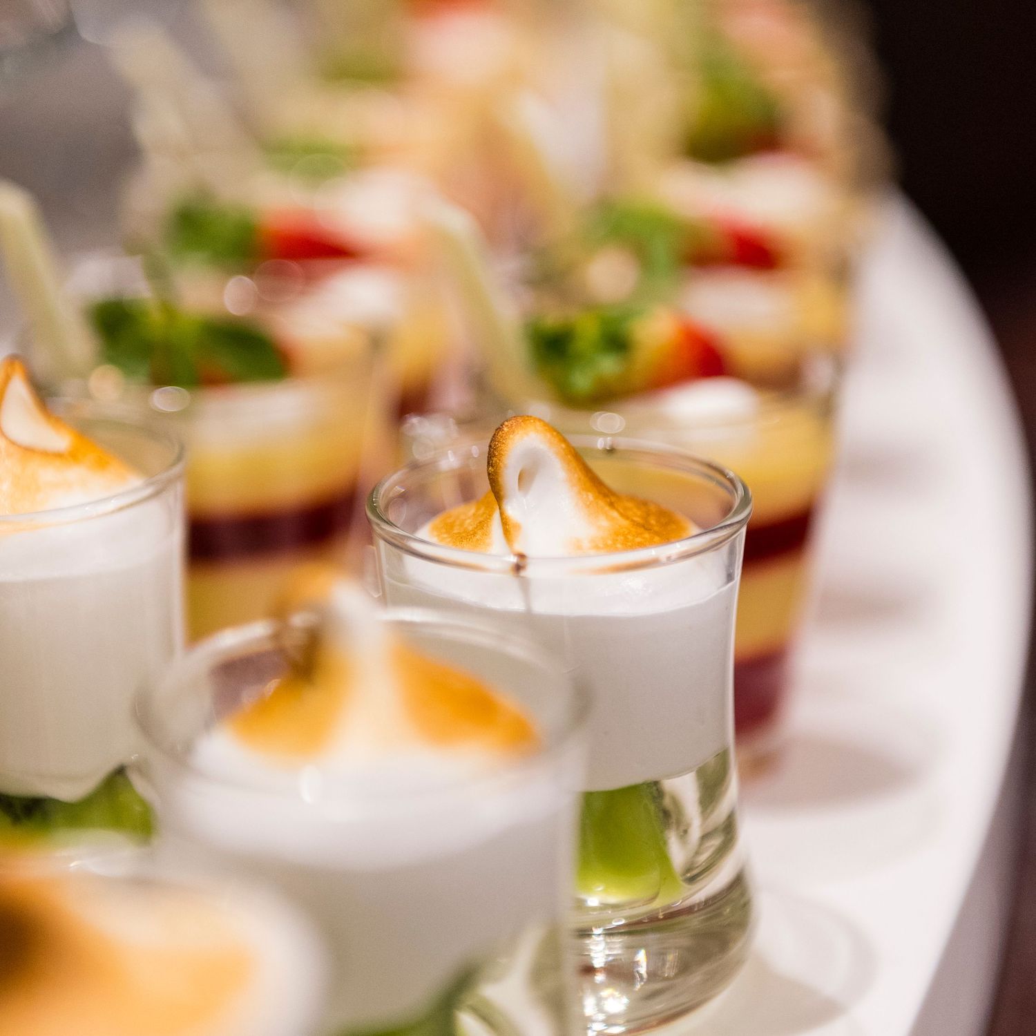 Artfully presented appetizers in small glass vessels with orange garnishes.