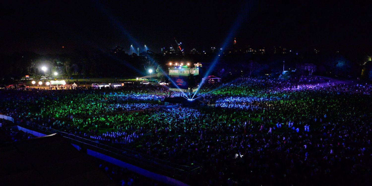 Concert arena filled with a sea of glowing blue and green lightsticks creating a mesmerizing illuminated atmosphere.