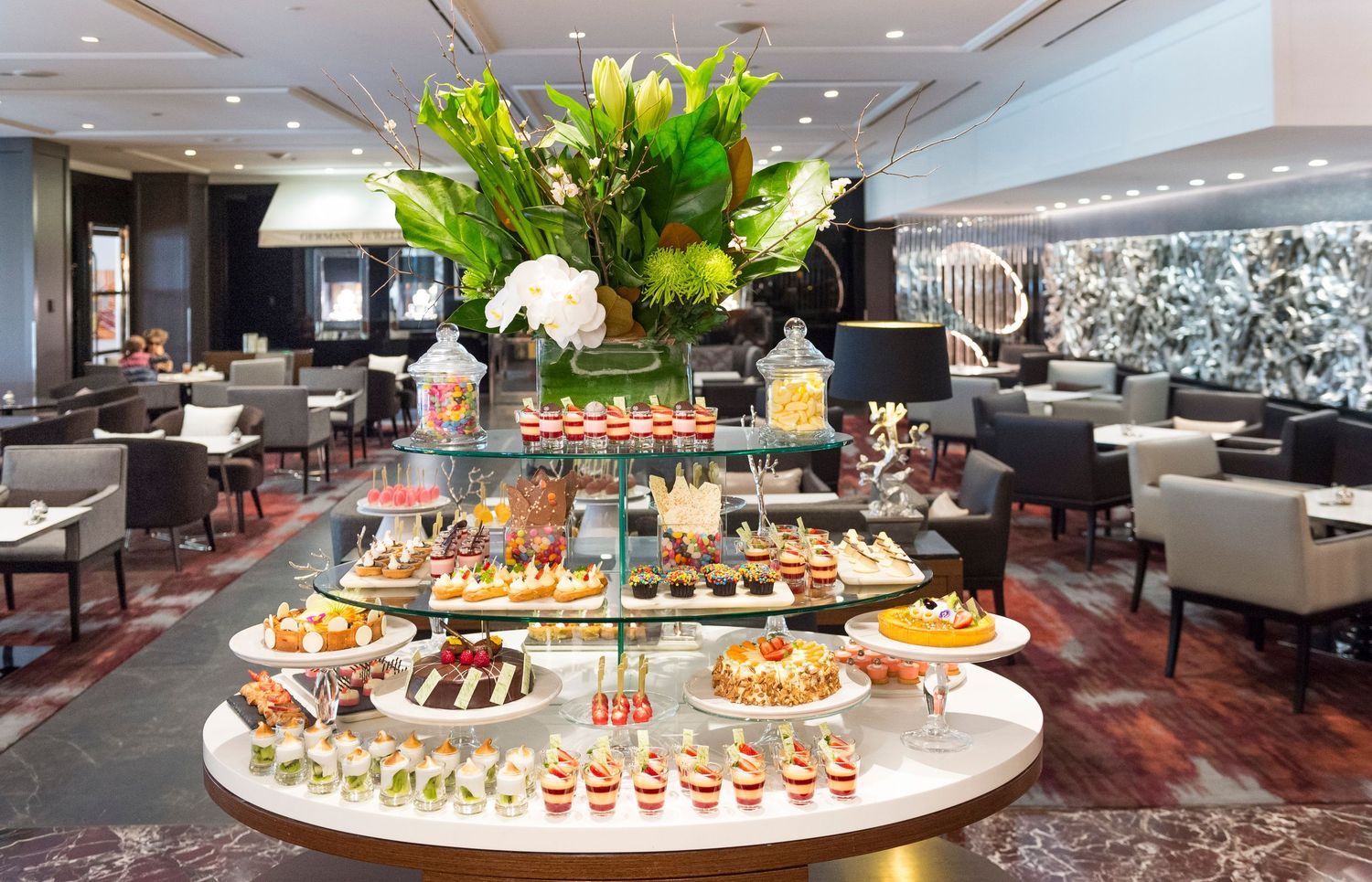 Elegant buffet display with colorful appetizers and fresh floral arrangements on marble countertops.