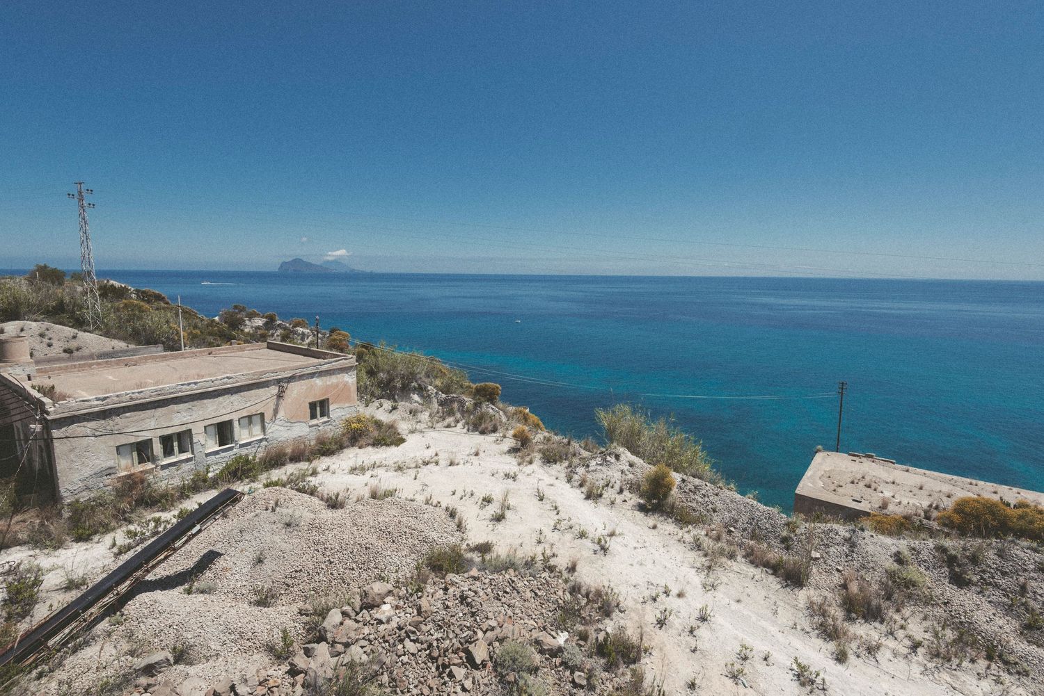 Panoramic view of a rugged coastal landscape with turquoise waters and rocky cliffs under bright blue skies.