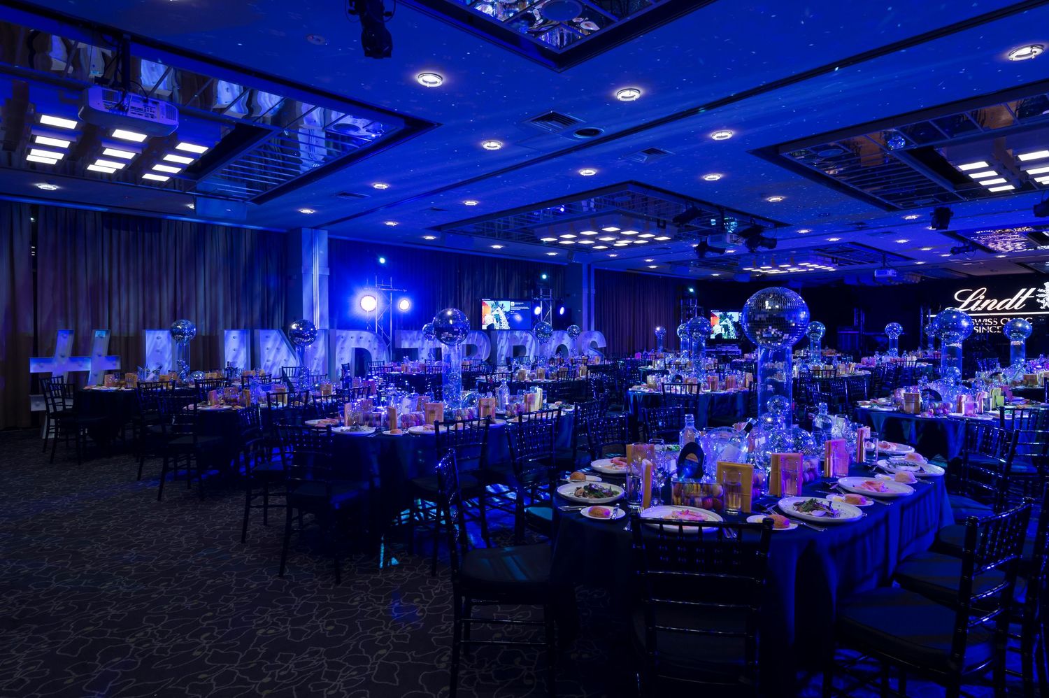 Large banquet hall illuminated in dramatic blue lighting with round tables set up for a formal event.
