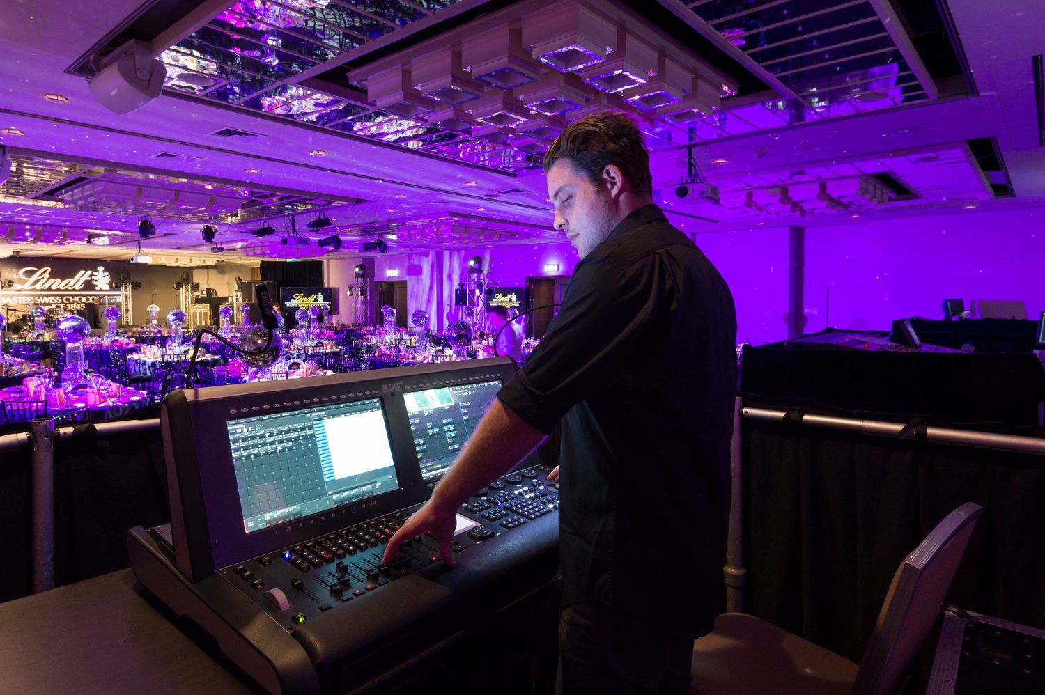 Professional event production setup with purple lighting and multiple control stations in a large venue space.