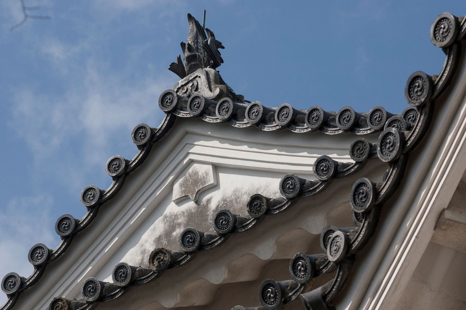 Traditional Japanese temple roofline with ornate curved tiles against blue sky.