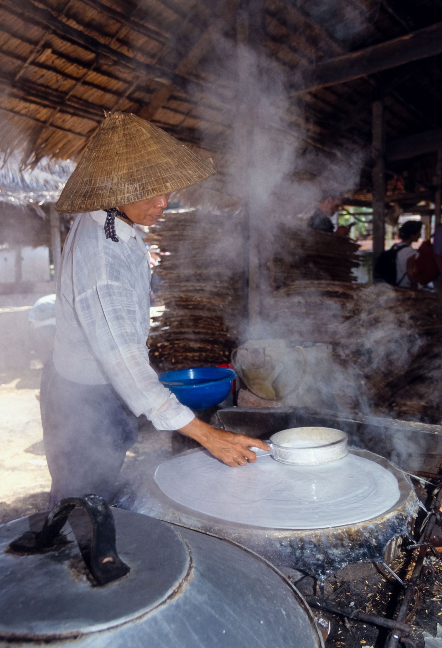 Steam rises from traditional rice paper making process on large circular cooking surface.