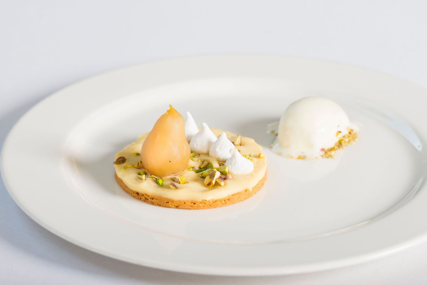 Minimalist plated dessert with peach-colored elements and white cream on pristine white dinnerware.