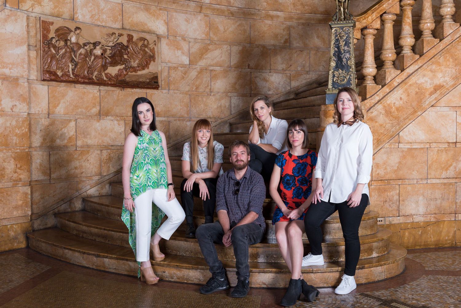 Group of people posing on stone staircase with decorative railing and wall art.