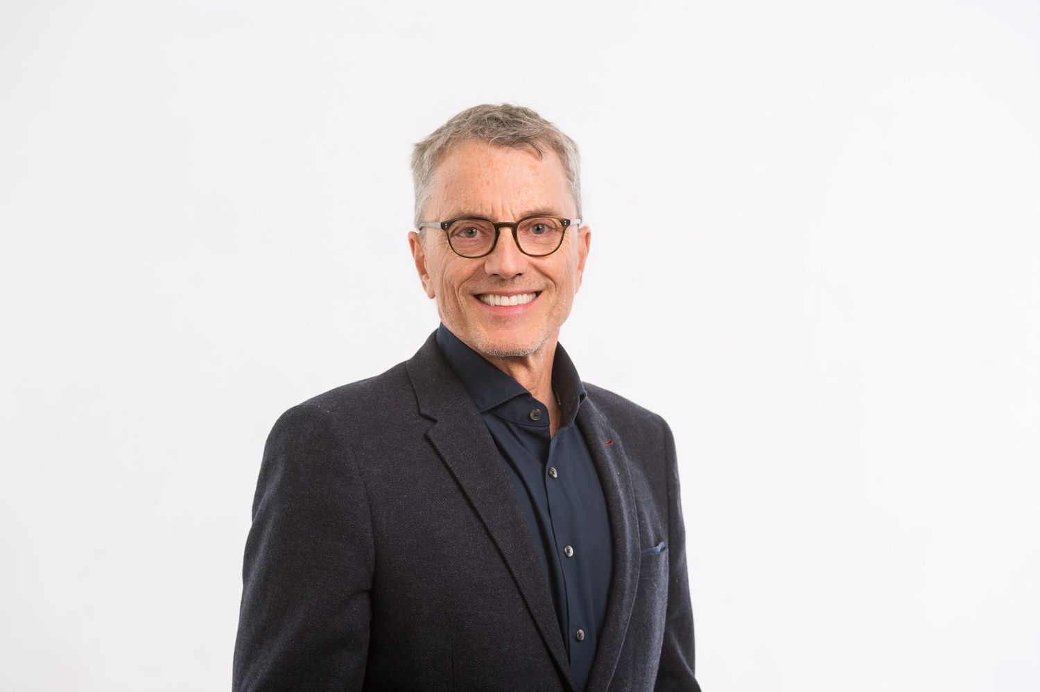 Professional headshots of person wearing dark suit and glasses.