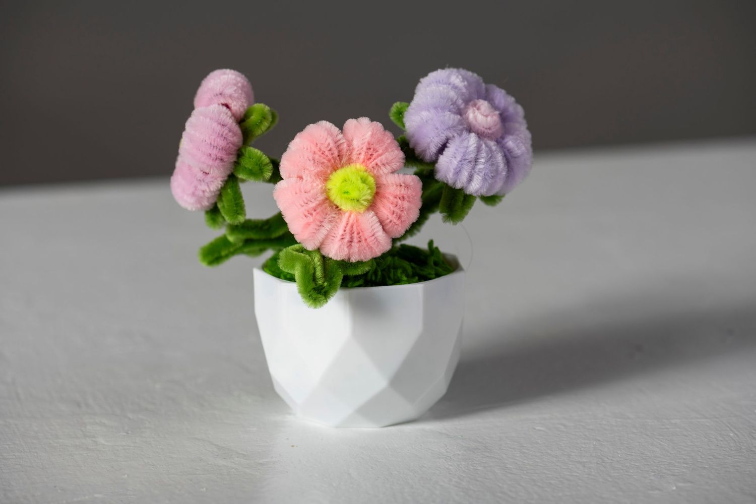 Small pink and purple flowers arranged in white ceramic egg shell vases on a gray surface.