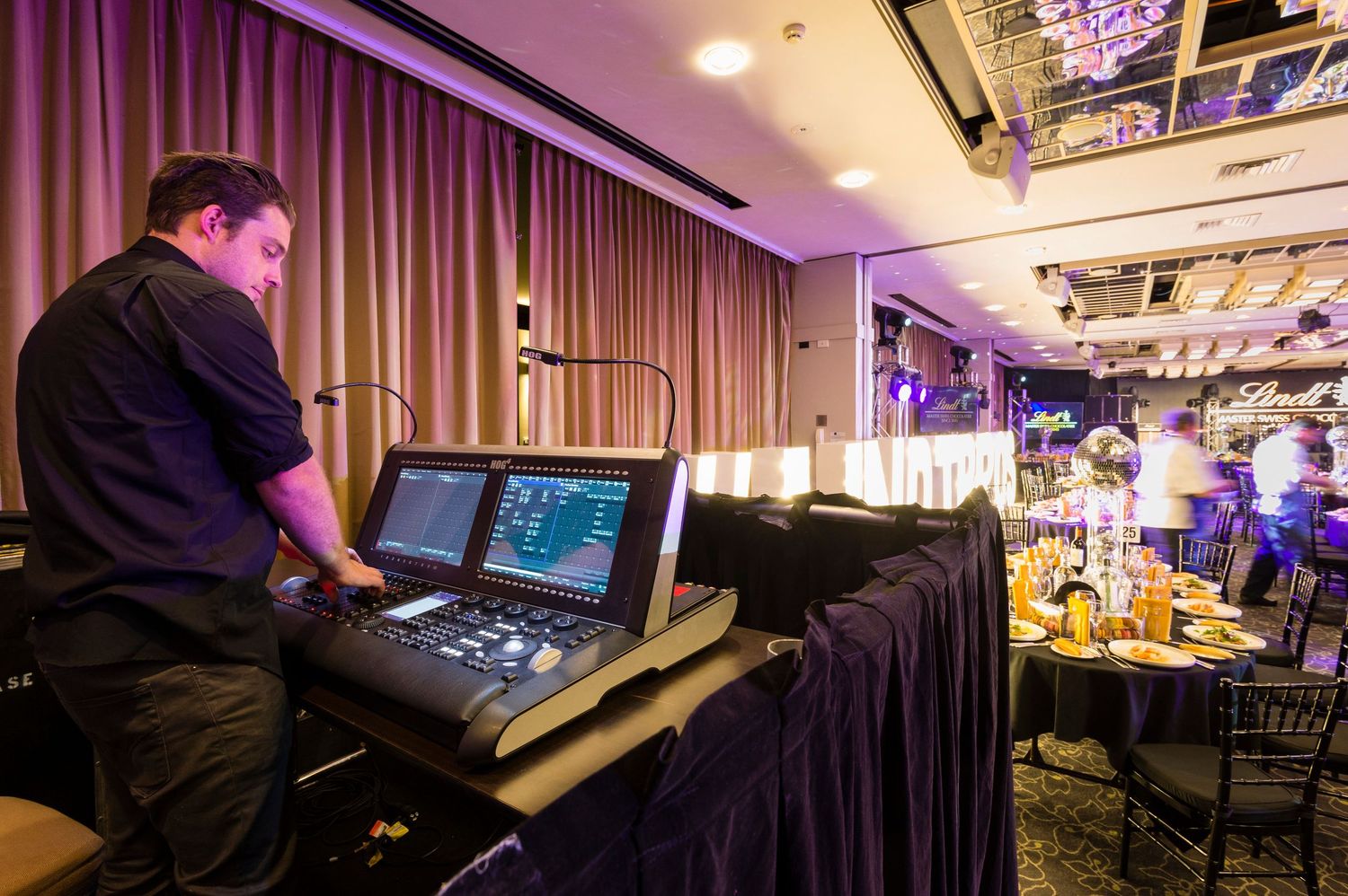 A dimly lit gaming setup with multiple monitors and purple ambient lighting in an entertainment room.