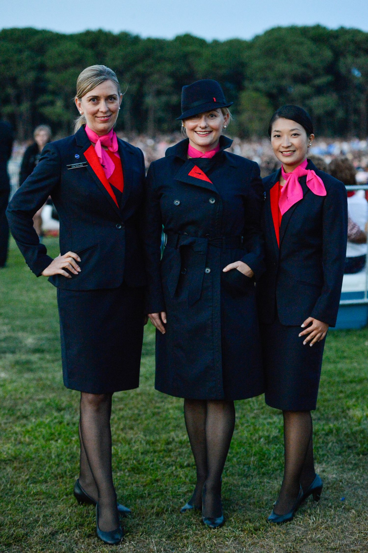 Flight attendants in navy blue uniforms and red scarves pose together on grass near an airfield.