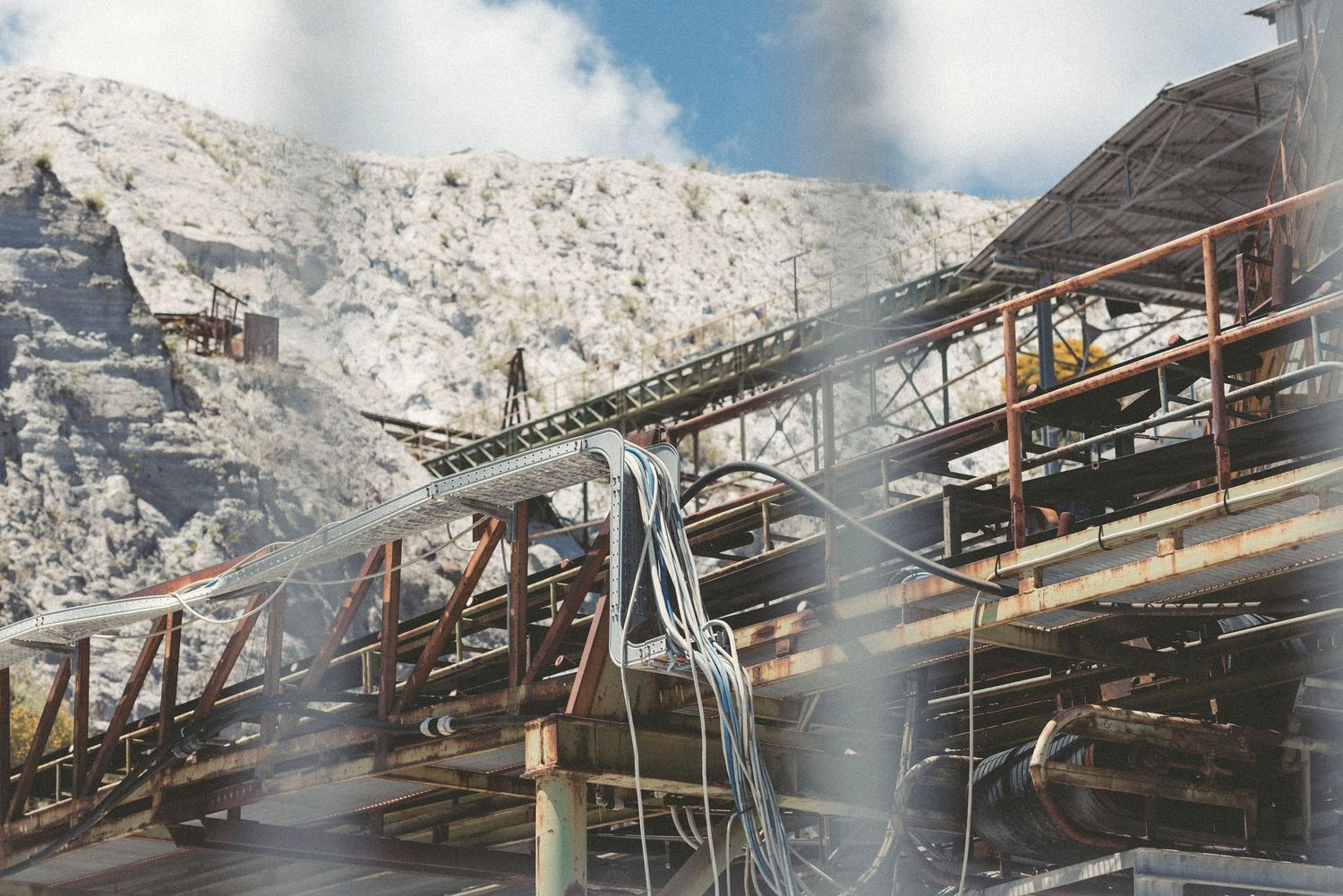 Industrial mining equipment and conveyor belts operate against a backdrop of white limestone quarry cliffs.