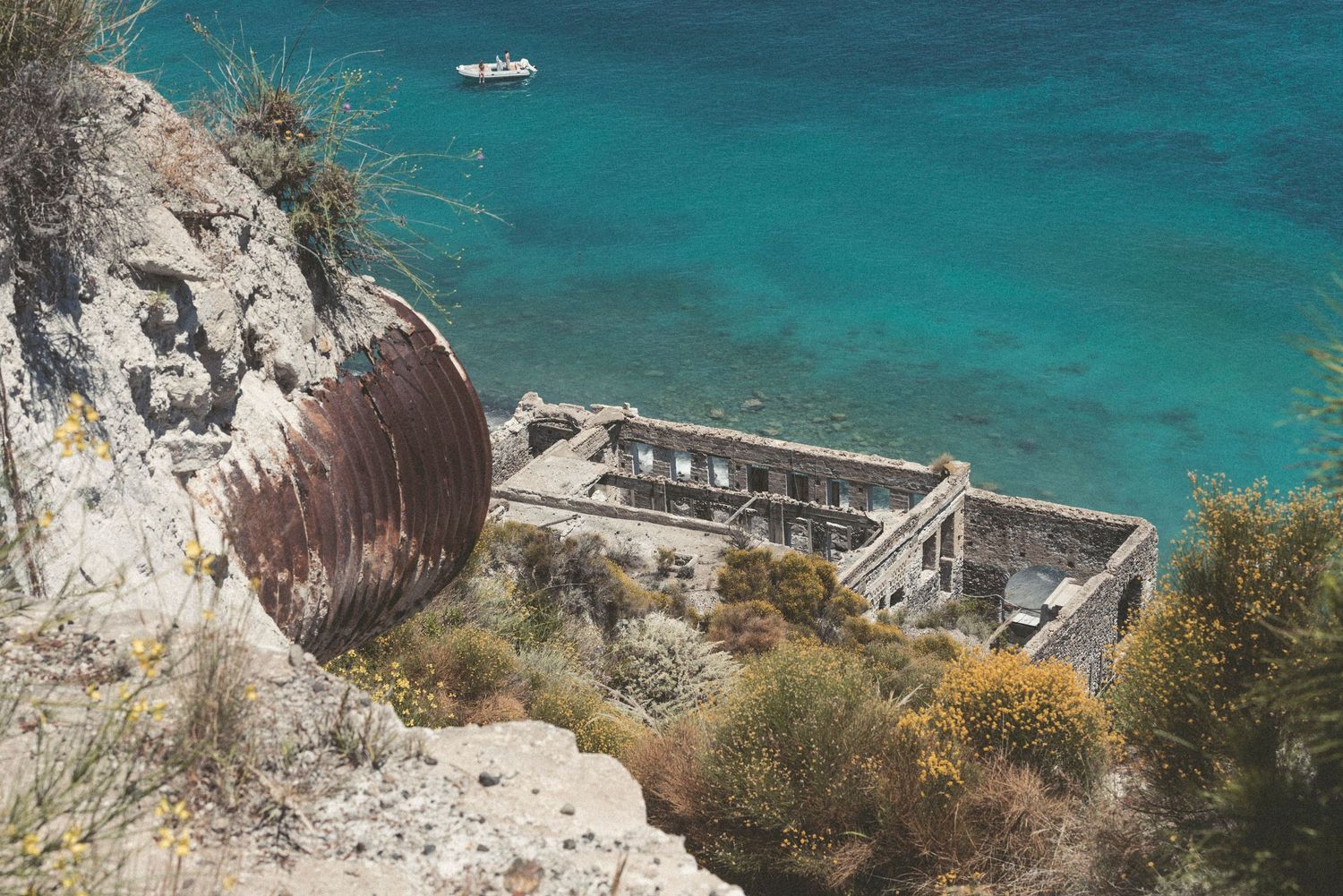 Aerial view of turquoise Mediterranean waters with boats anchored near rocky coastal cliffs and beaches.