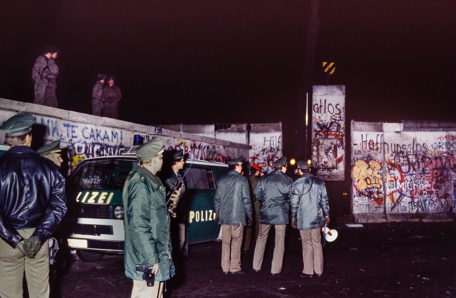 Protest signs and banners displayed in a row at night with people gathered around them.