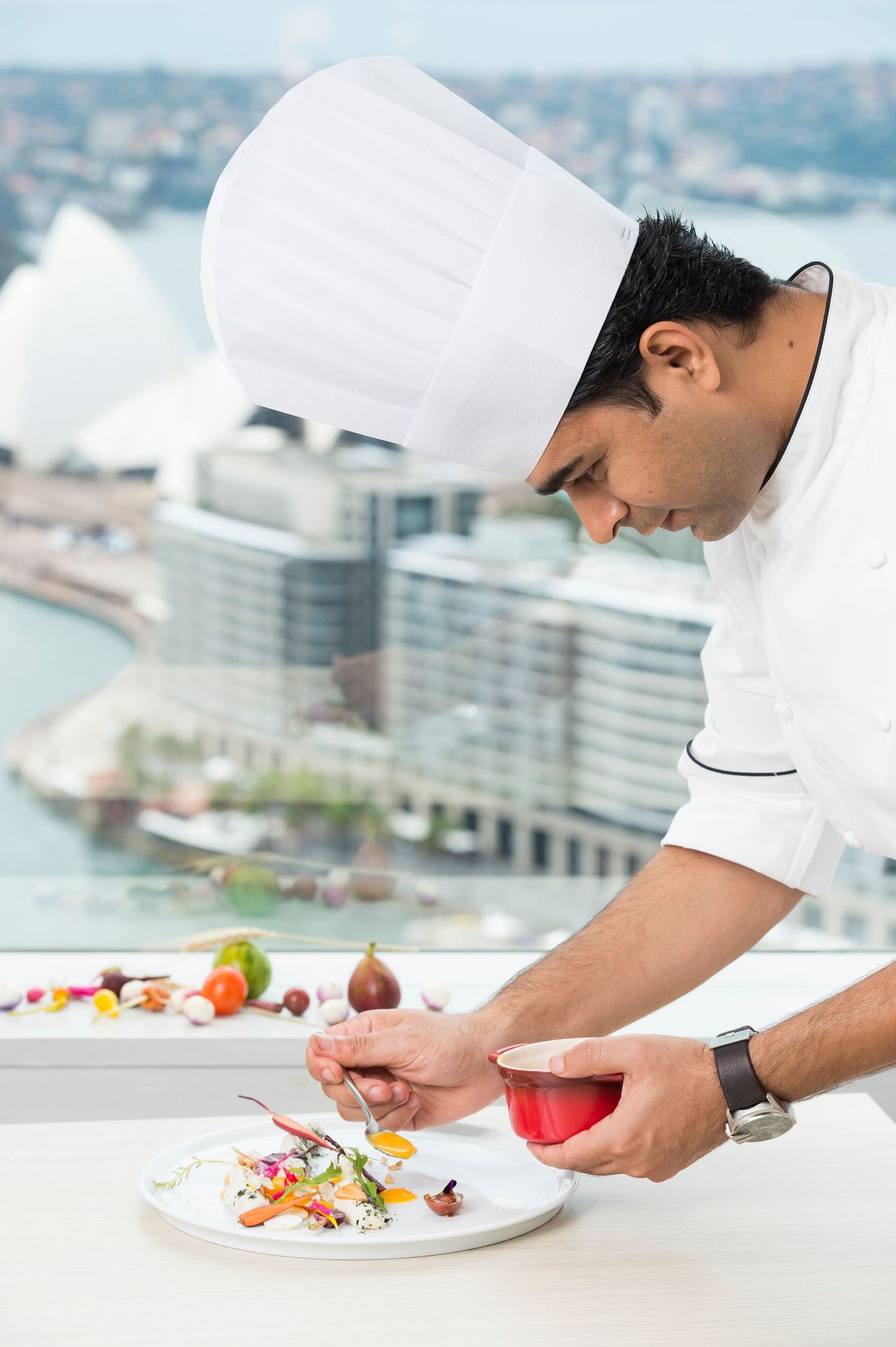 Chef in white uniform plating dishes with precision in modern restaurant kitchen.