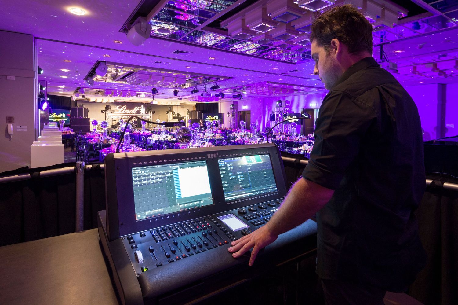 Audio engineer working at professional mixing console in purple-lit recording studio environment.