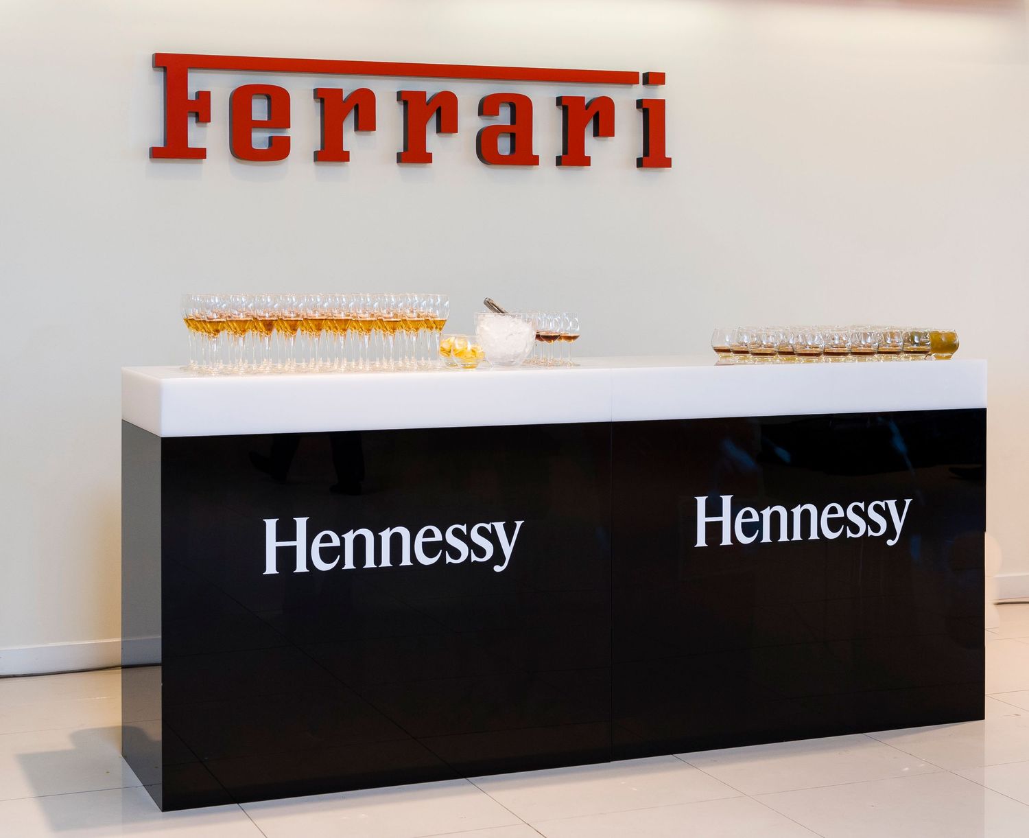 A collection of luxury brand display signs including Ferrari and Hennessy logos mounted on sleek black platforms.