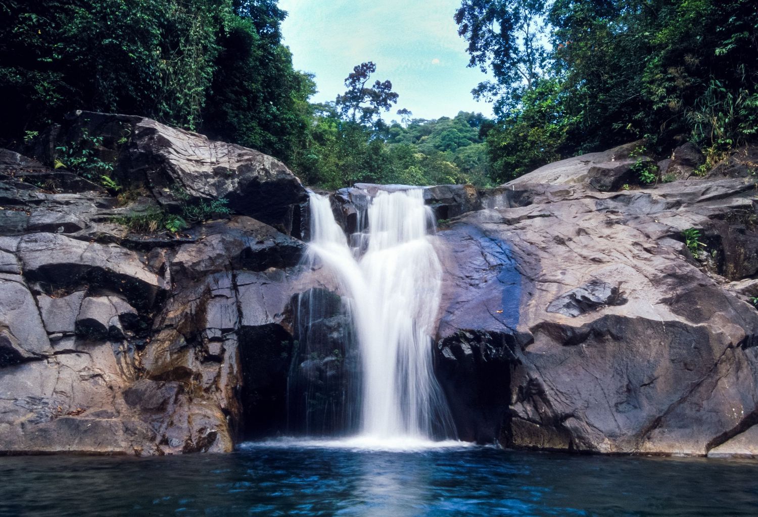 Scenic waterfall cascades over rocky terrain in a lush forest setting.