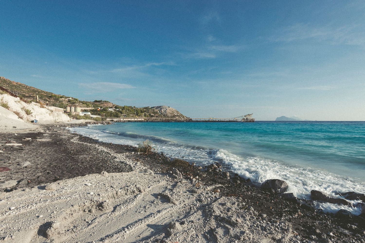 Scenic coastal landscape with turquoise waters and rocky cliffs along a Mediterranean beach under bright blue skies.