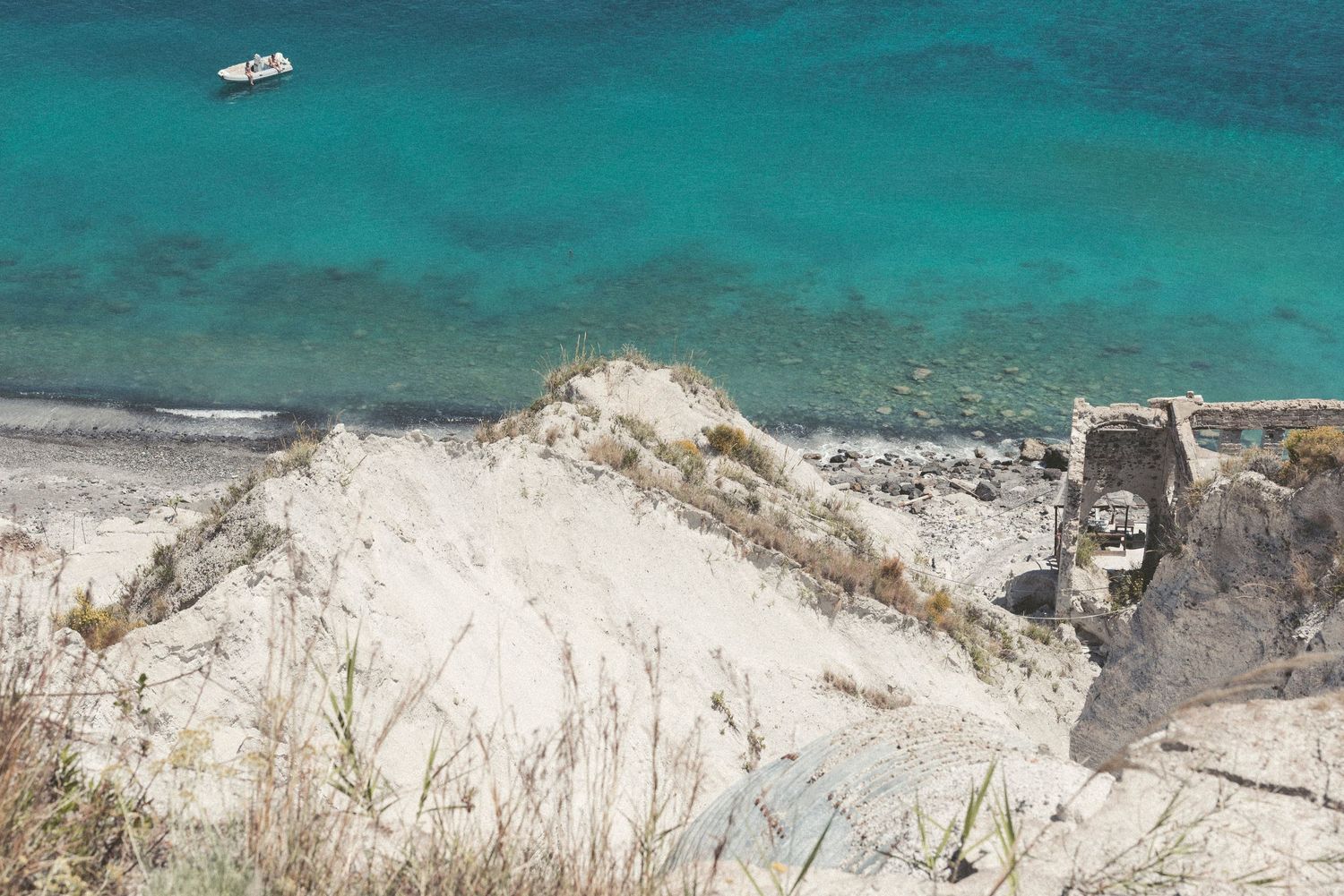 Aerial view of turquoise Mediterranean waters with white limestone cliffs and a small boat in the distance.