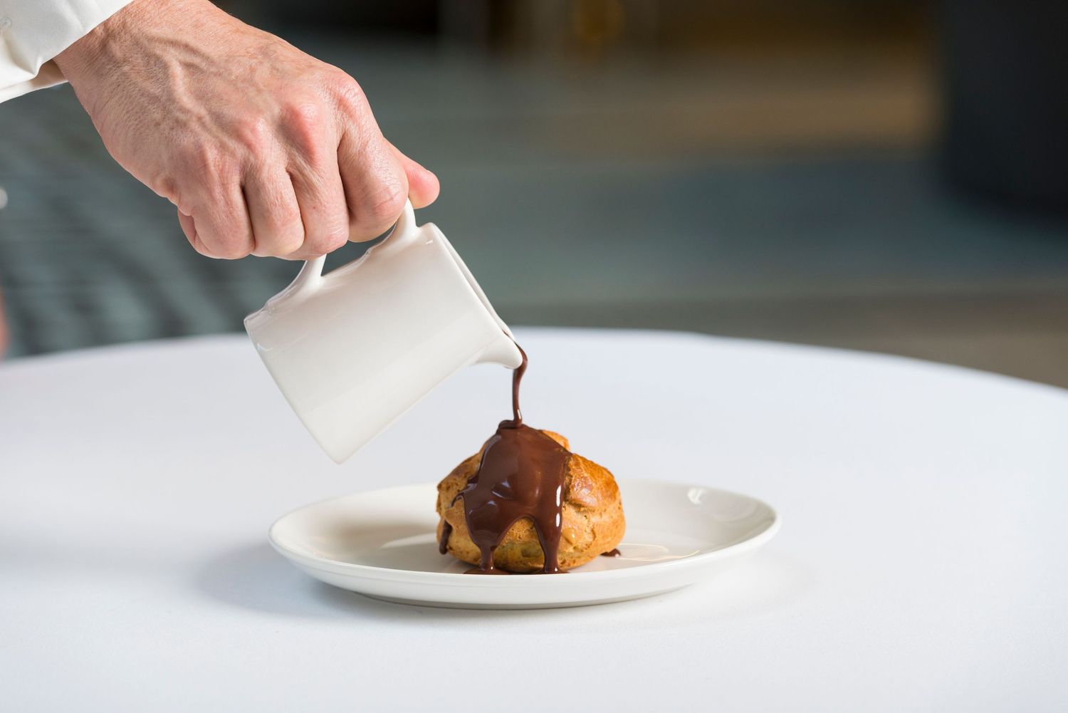 Plating of an elegant dessert with sauce being drizzled on white dishes.