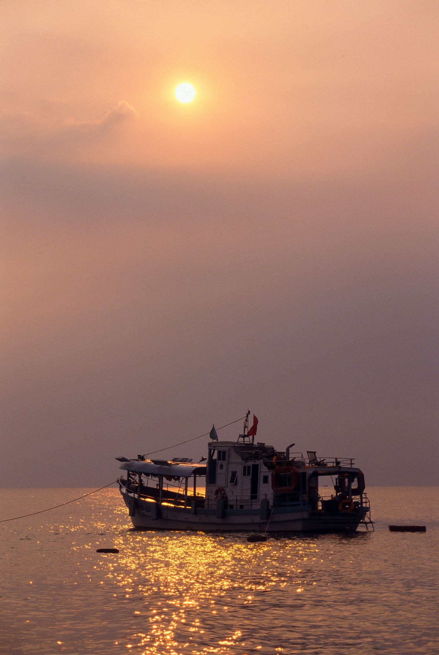 Fishing boats silhouetted against a golden sunset over calm ocean waters.