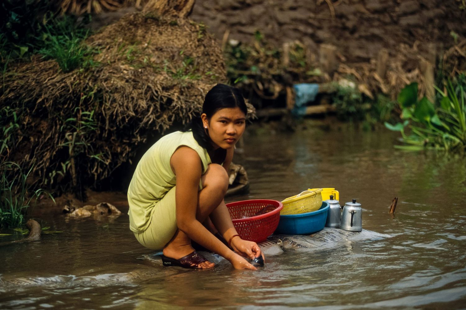 People washing dishes and clothes along a riverbank in rural Southeast Asia.