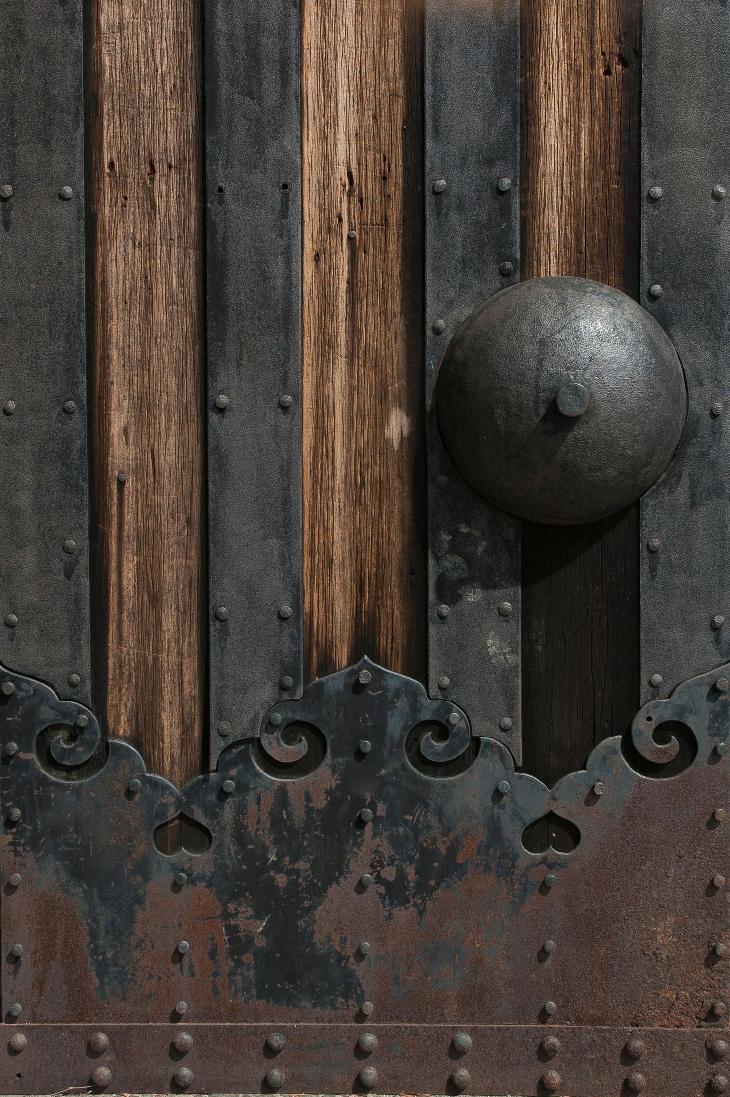 Vintage wooden and metal wall panel with dark patina and decorative rivets.