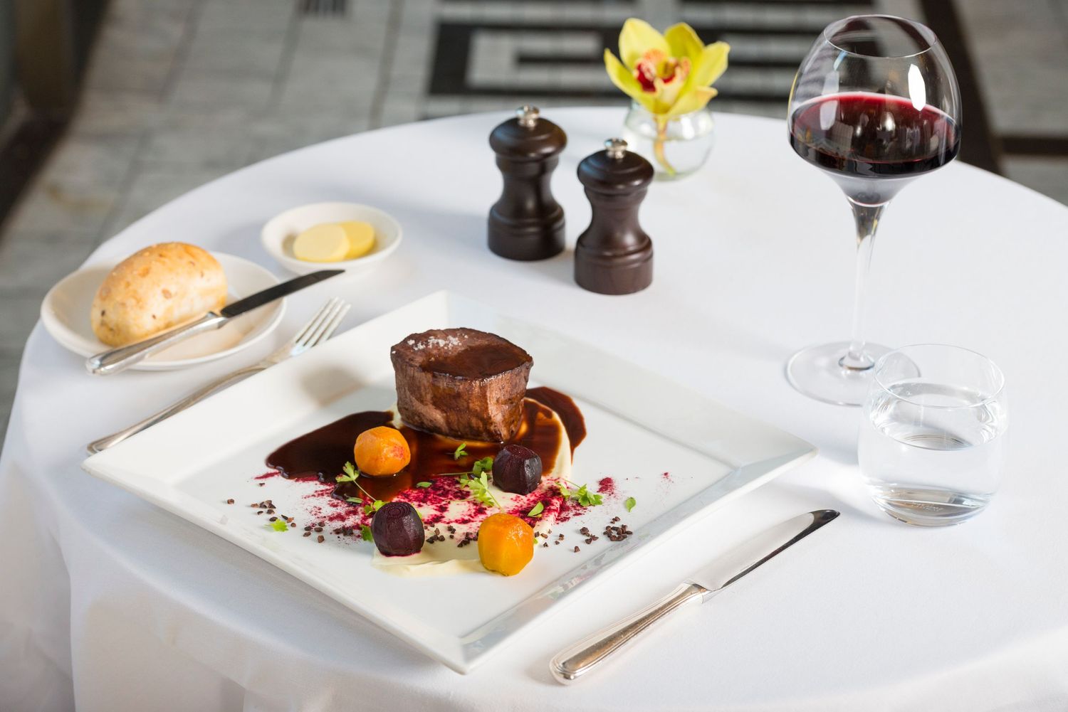Fine dining table setting with yellow orchid, wine glasses, and multiple course presentation.