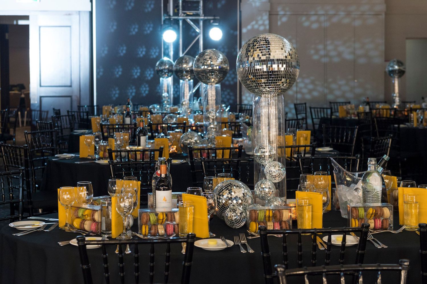 Modern styled dining room venue with black chairs and yellow table settings illuminated by decorative crystal light fixtures.