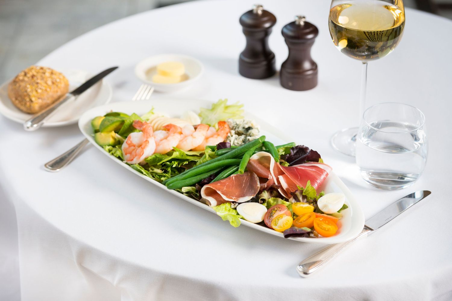 Fine dining plates featuring salads and seafood dishes arranged on white tablecloth.