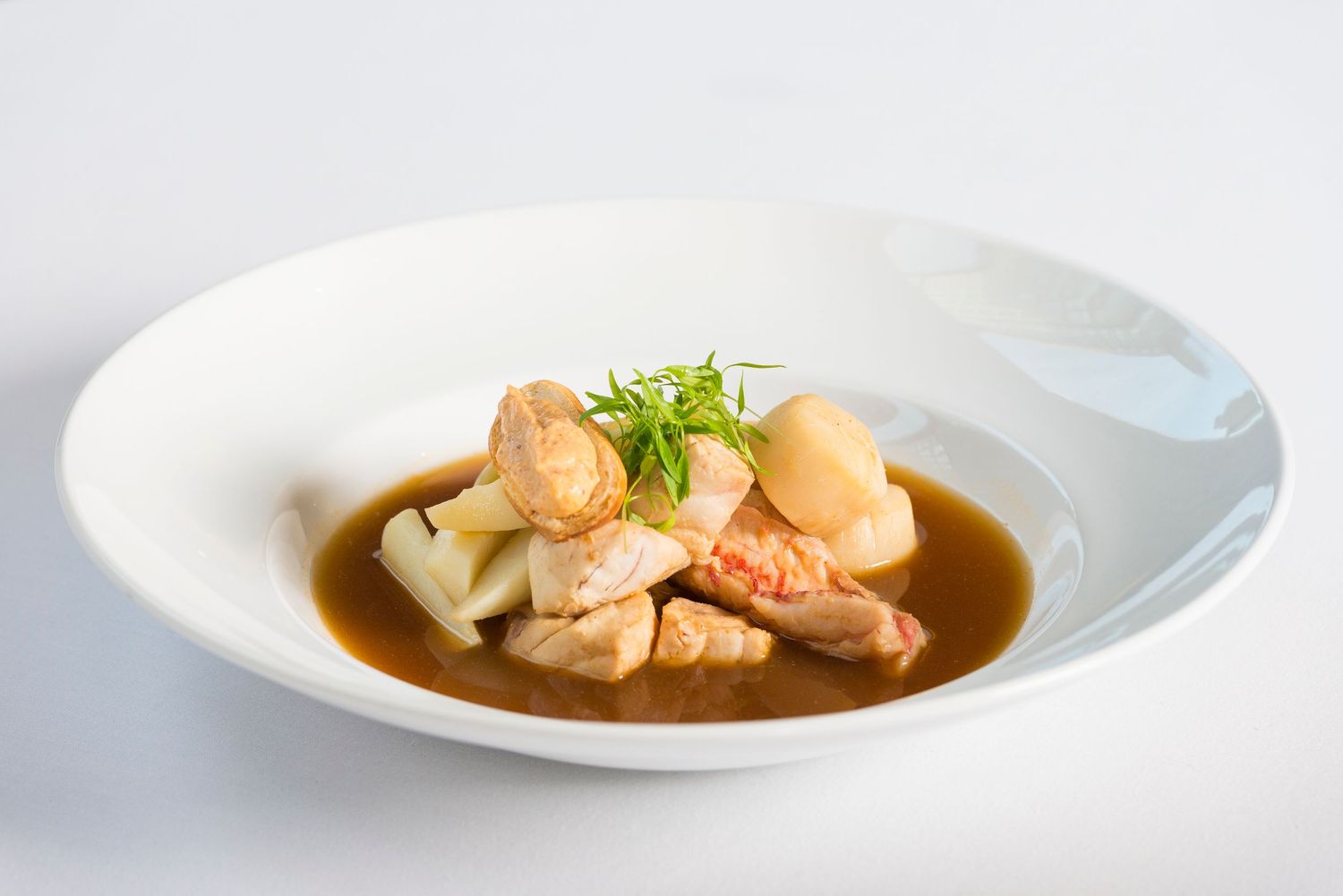 Plated fish dish in brown sauce with fresh herbs on white ceramic plate.