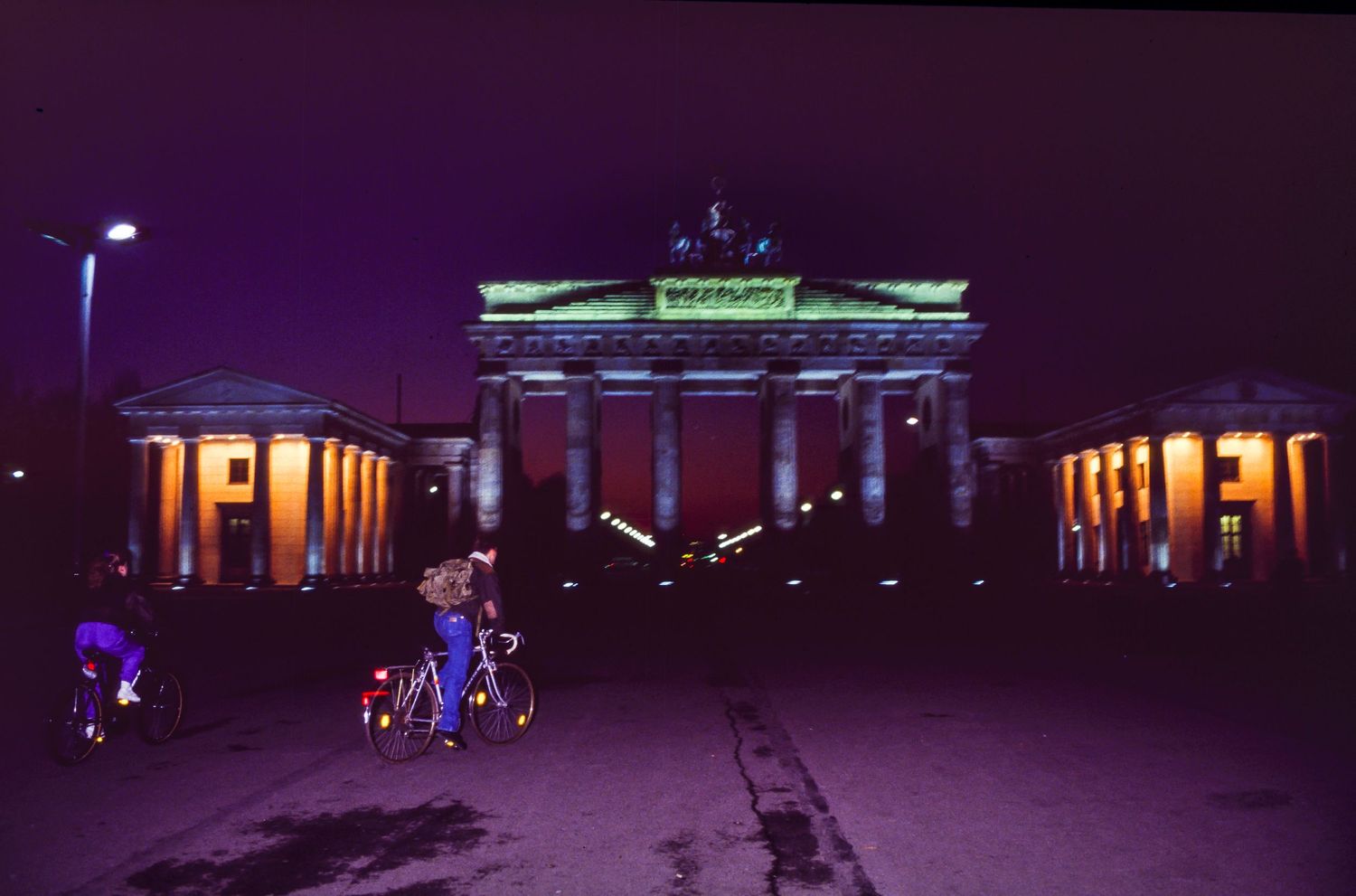 Illuminated Brandenburg Gate in Berlin at night with purple and orange lighting effects.