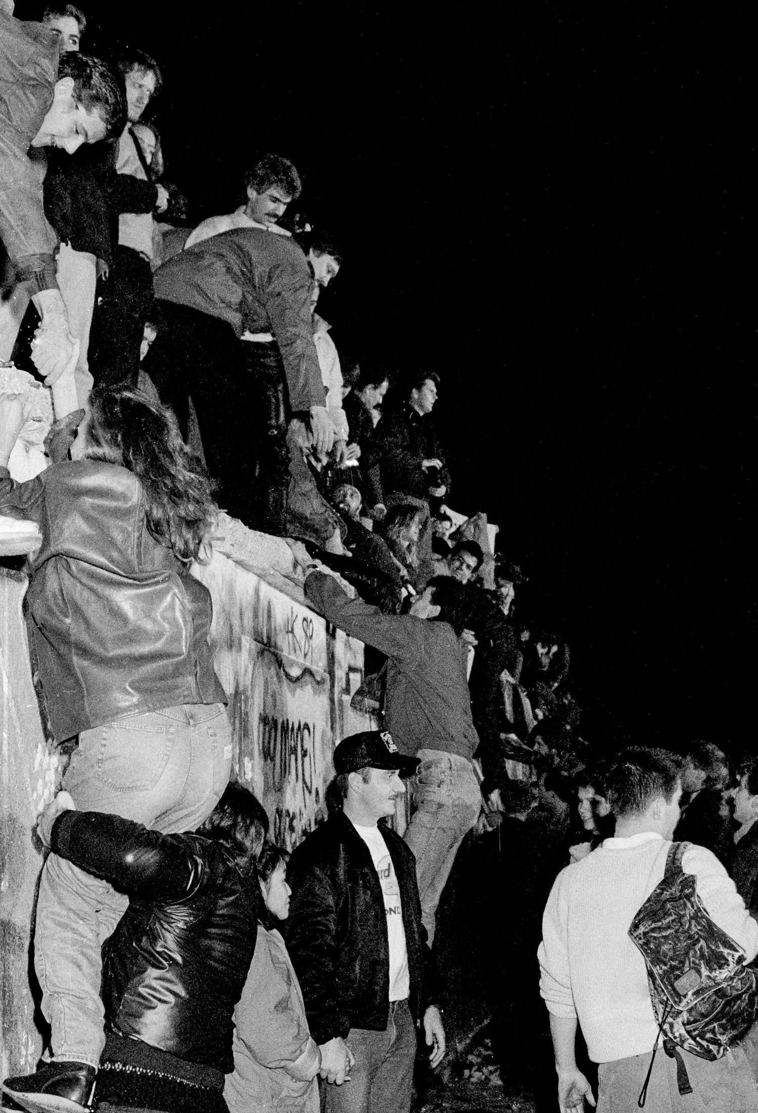 Black and white photo of people climbing and gathering on the Berlin Wall during its fall.