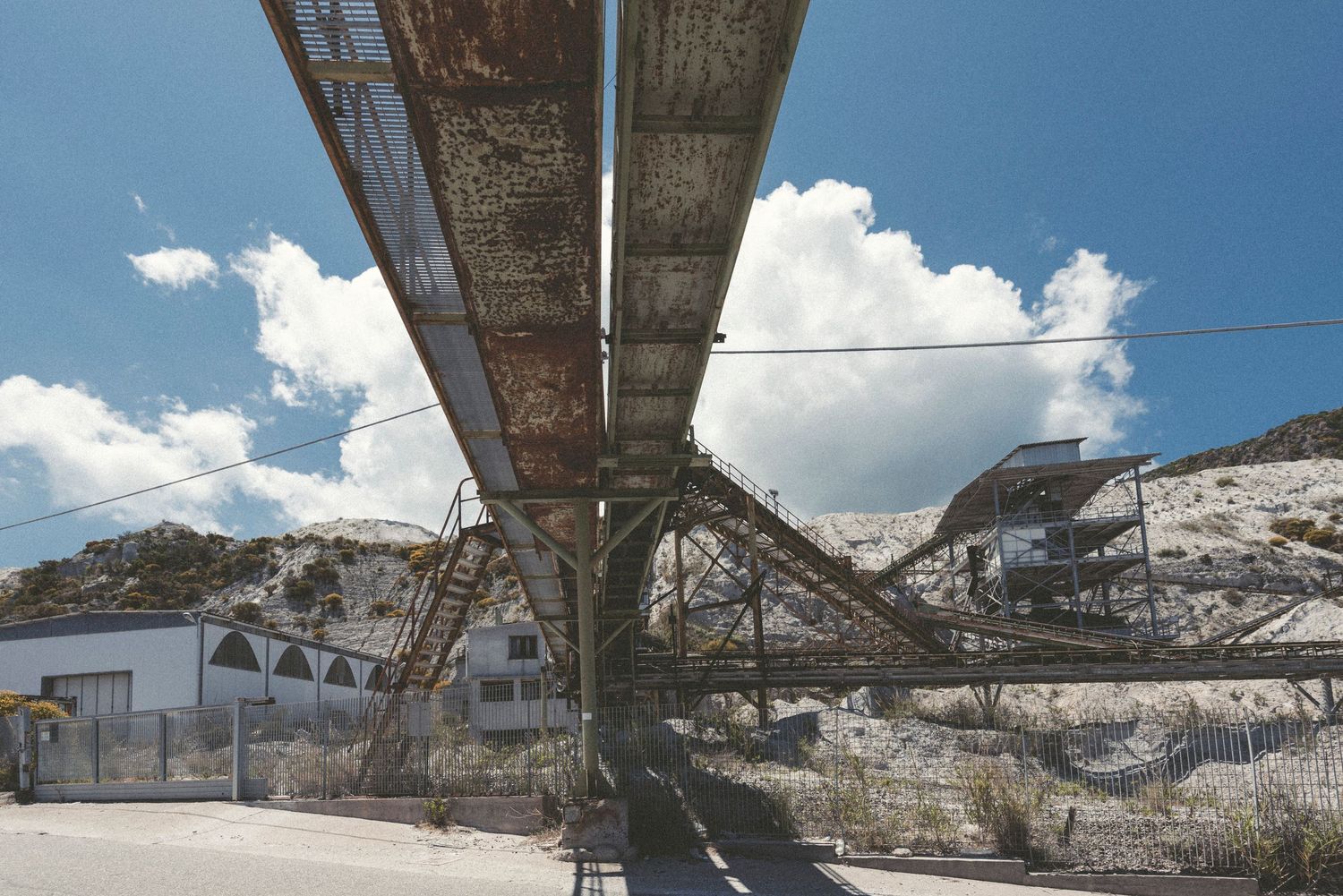 Industrial mining facility with overhead conveyor systems and equipment in a rocky quarry landscape.