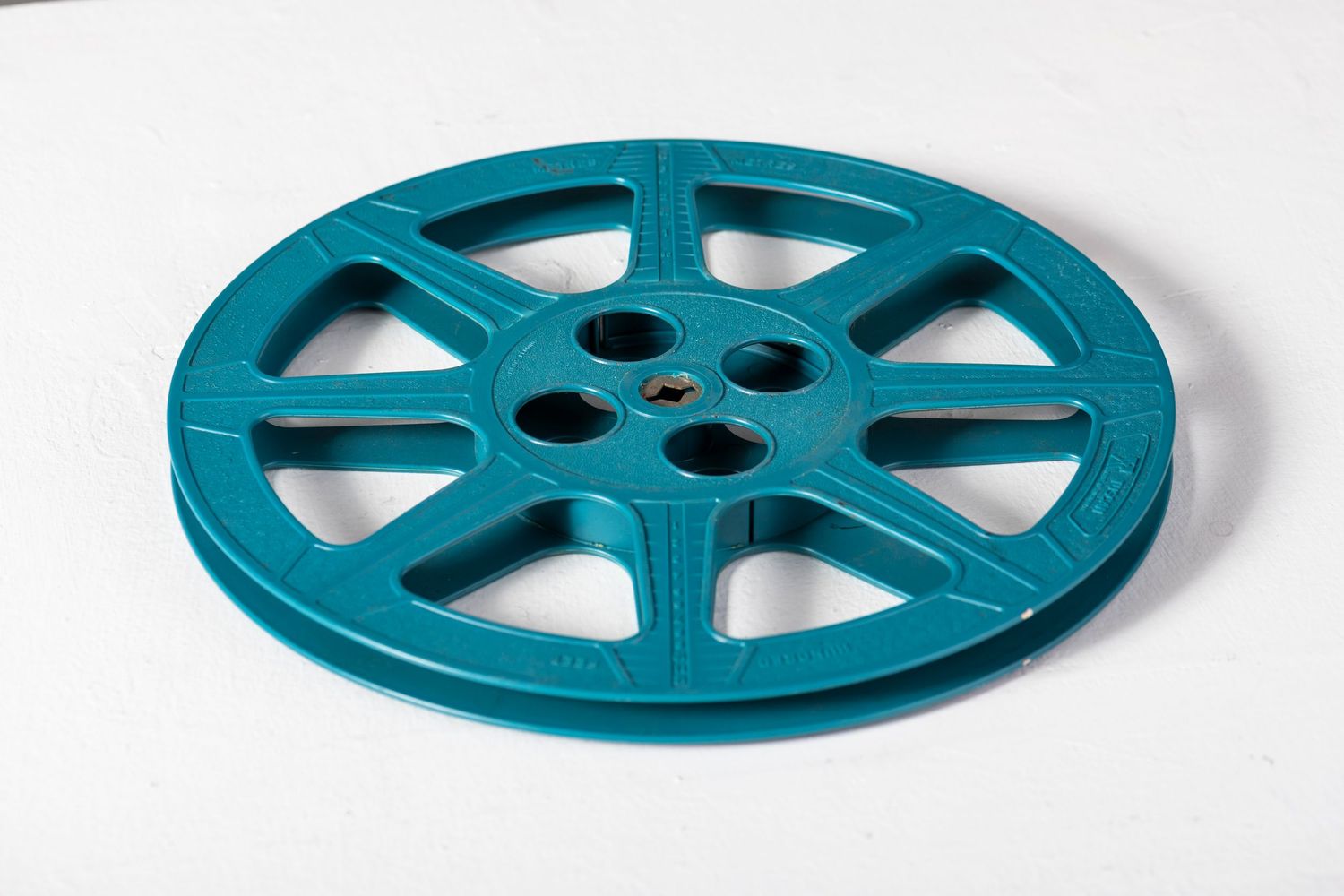 Teal blue movie film reel shown from multiple angles on a white background.