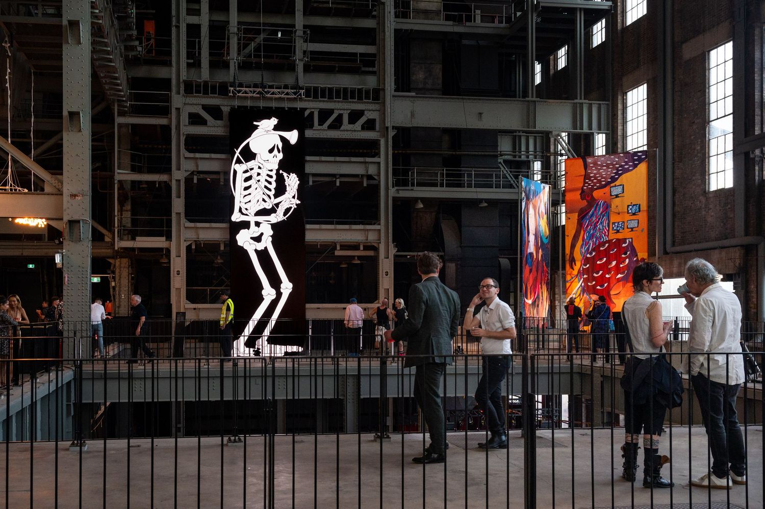 Large industrial exhibition space with visitors exploring art installations.