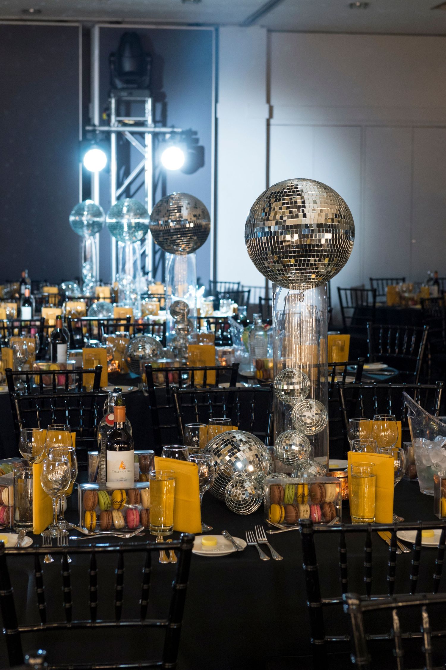 Elegant event venue with disco ball centrepieces, black chairs and yellow menu cards set for a formal sponsored night gala.