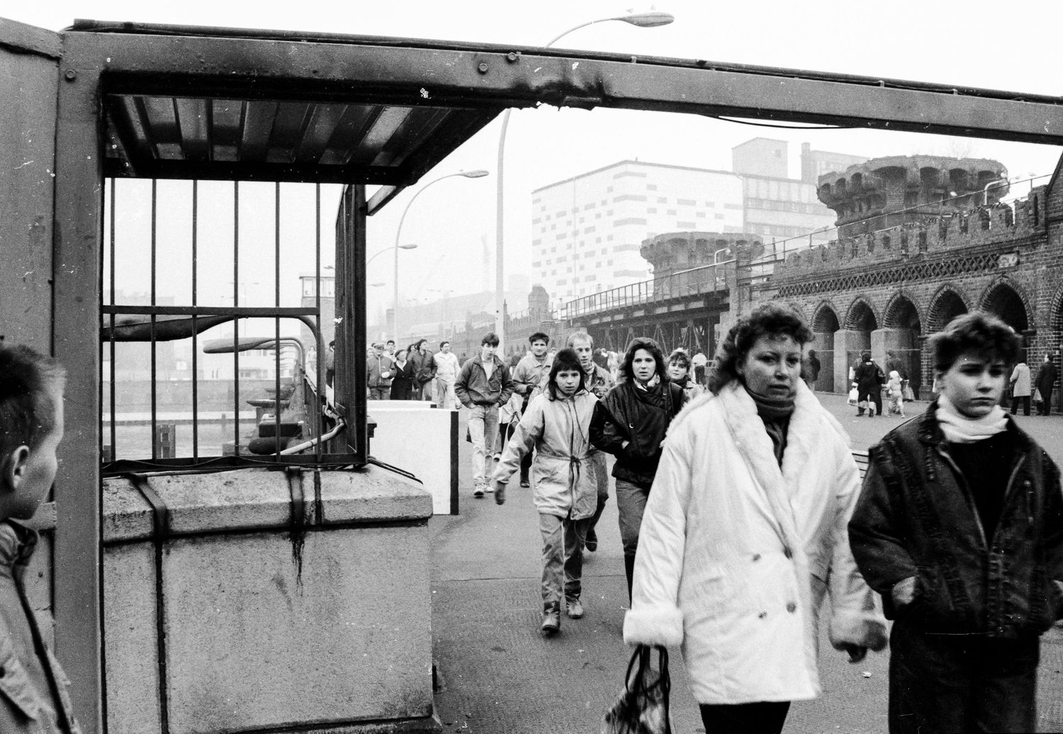 People walking near concrete barriers and guard posts along the Berlin Wall.
