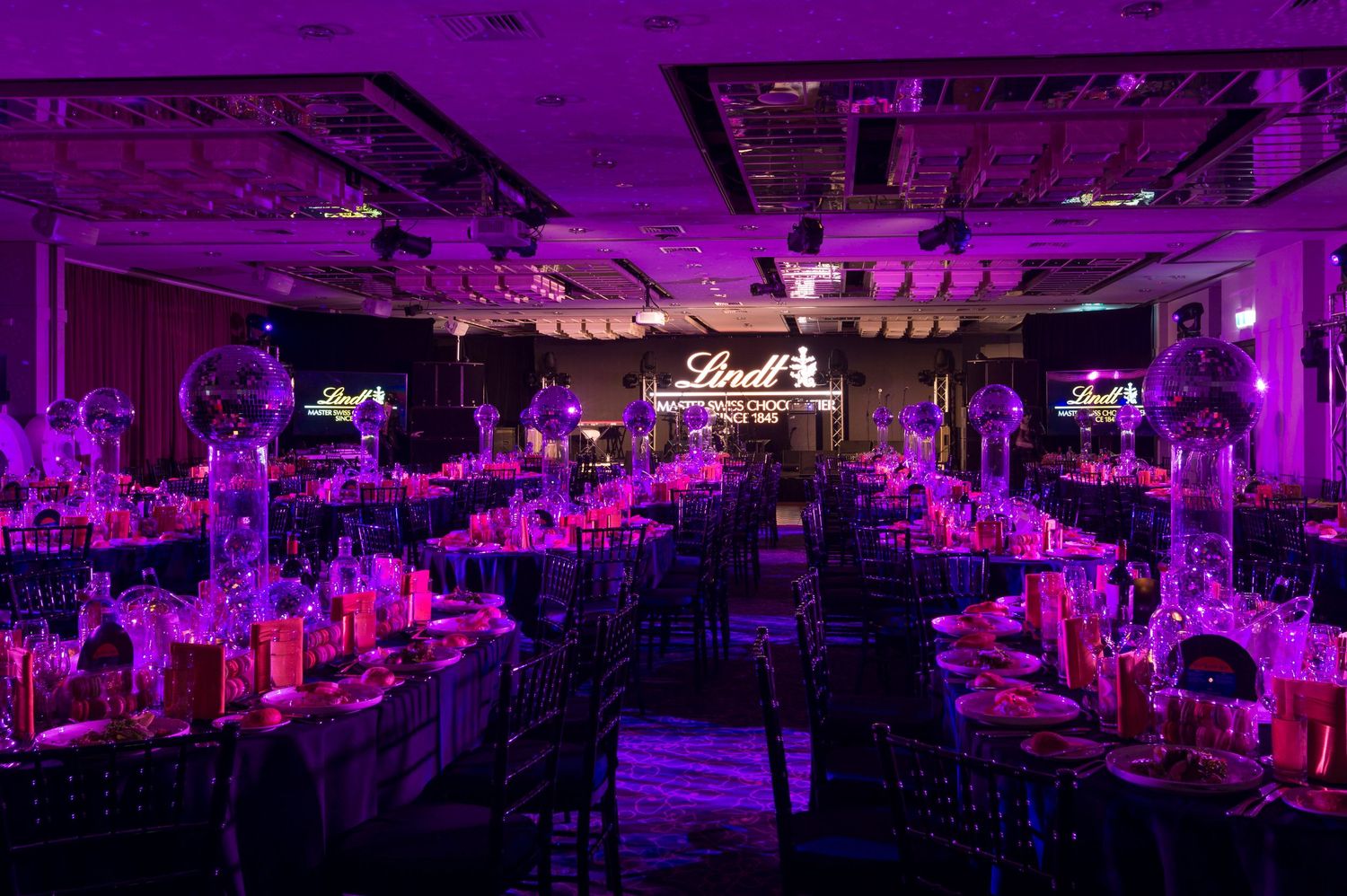 Elegant ballroom with purple uplighting illuminates round dining tables set for a formal evening event.