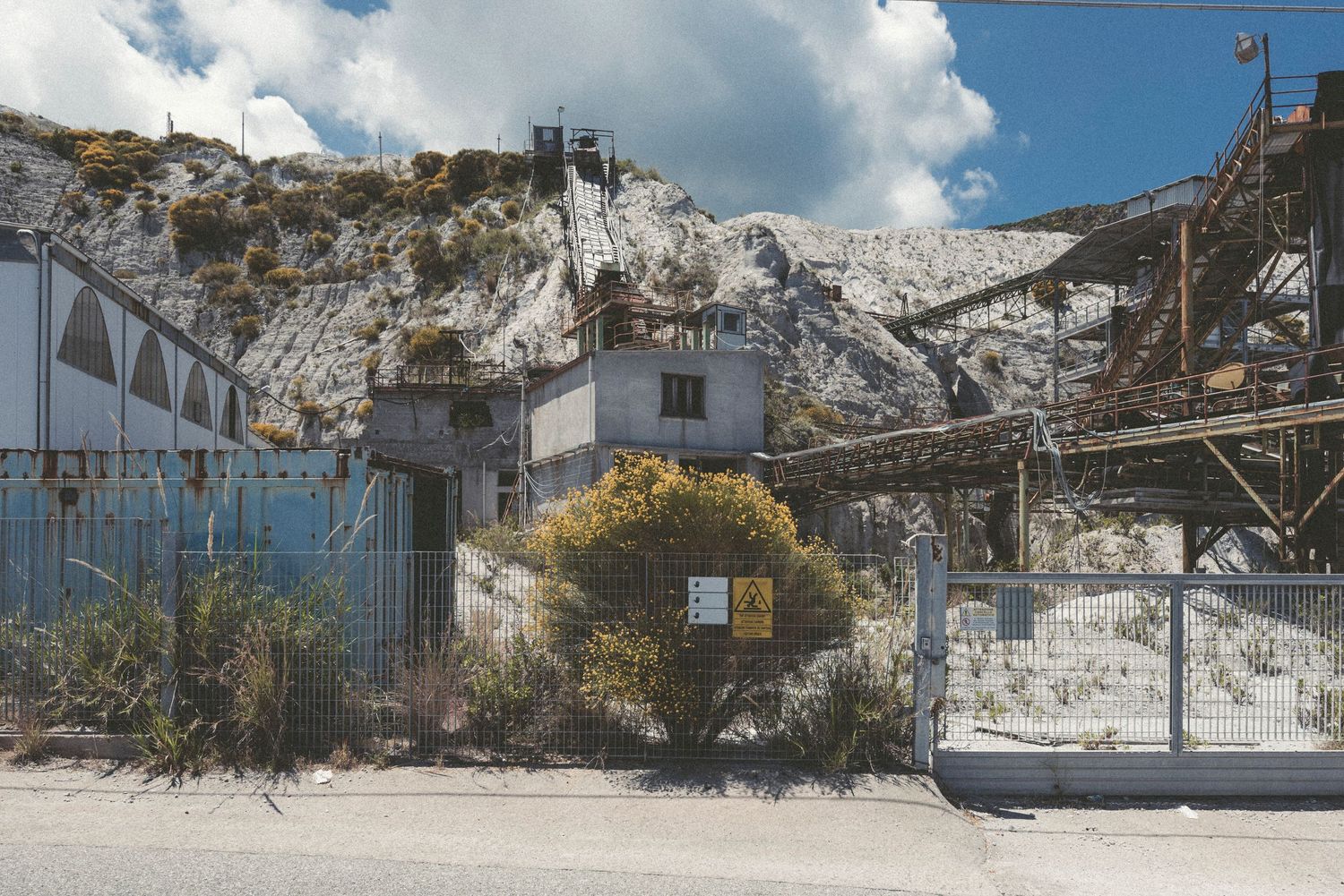 Panoramic view of an industrial mining site with white limestone quarry walls and processing equipment under cloudy skies.