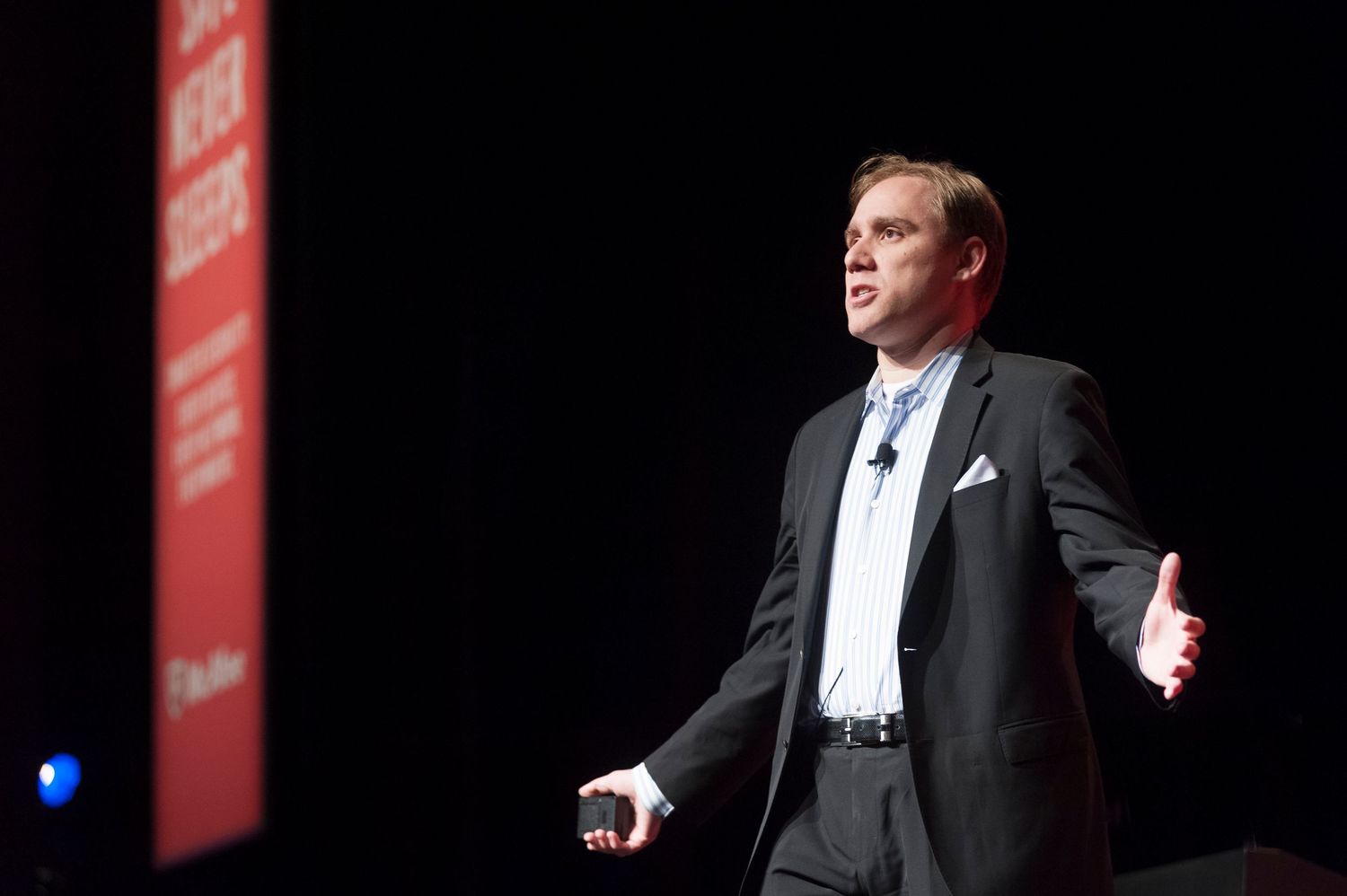 A speaker presents on a darkened stage with dramatic red lighting and professional attire at Sydney International Convention Centre.