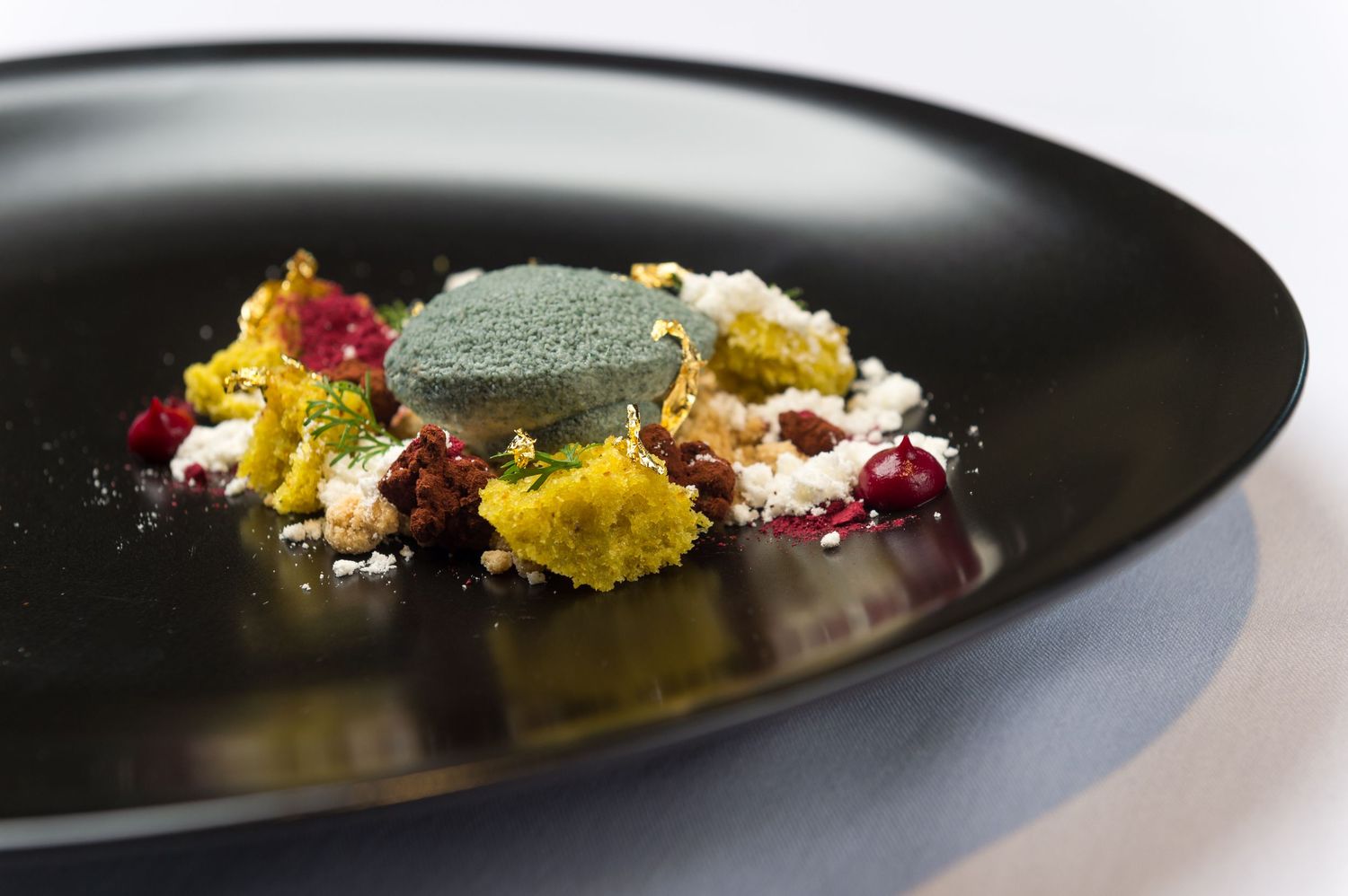 Elegant dessert plated on black slate with colorful edible flowers and delicate garnishes.