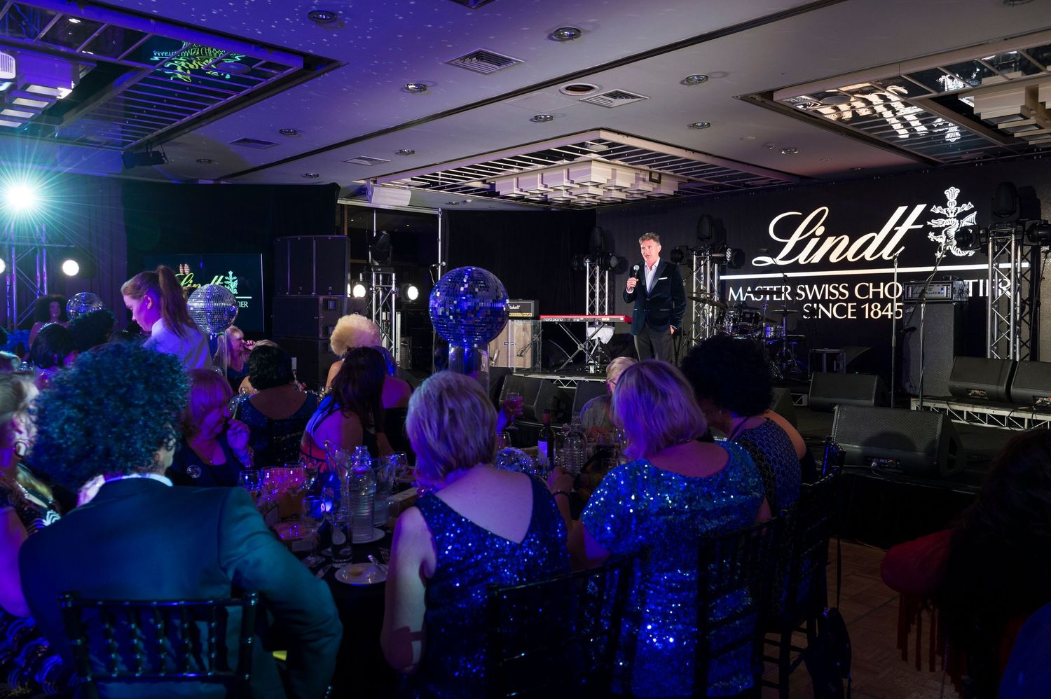 A crowd gathers in a dark venue with blue lighting and a Lindt logo display for an evening event.