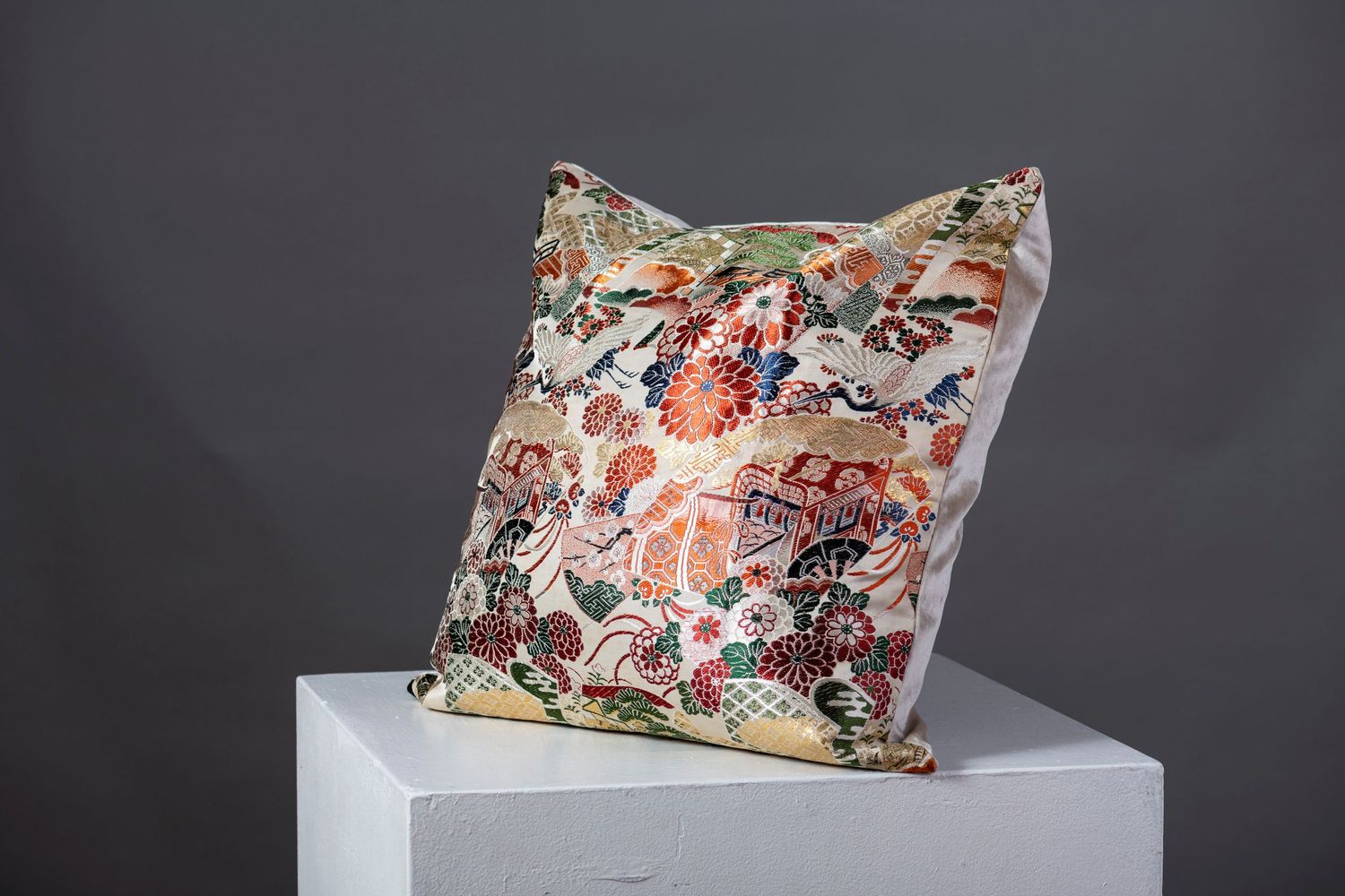 Decorative floral pattern throw pillows displayed on white pedestals against a dark background.