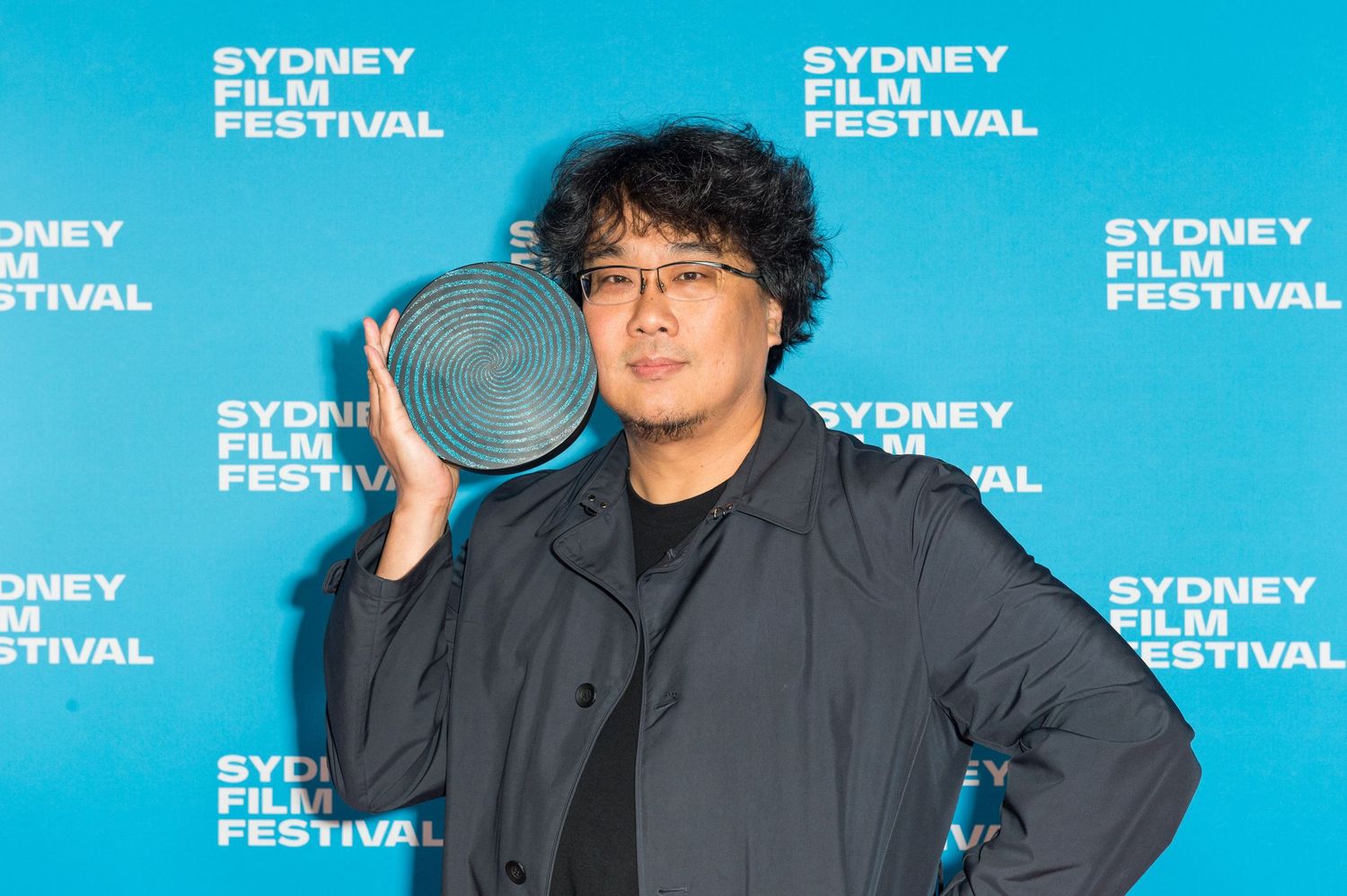 Three people stand together at a Sydney Film Festival event against a blue backdrop with repeating festival logos.